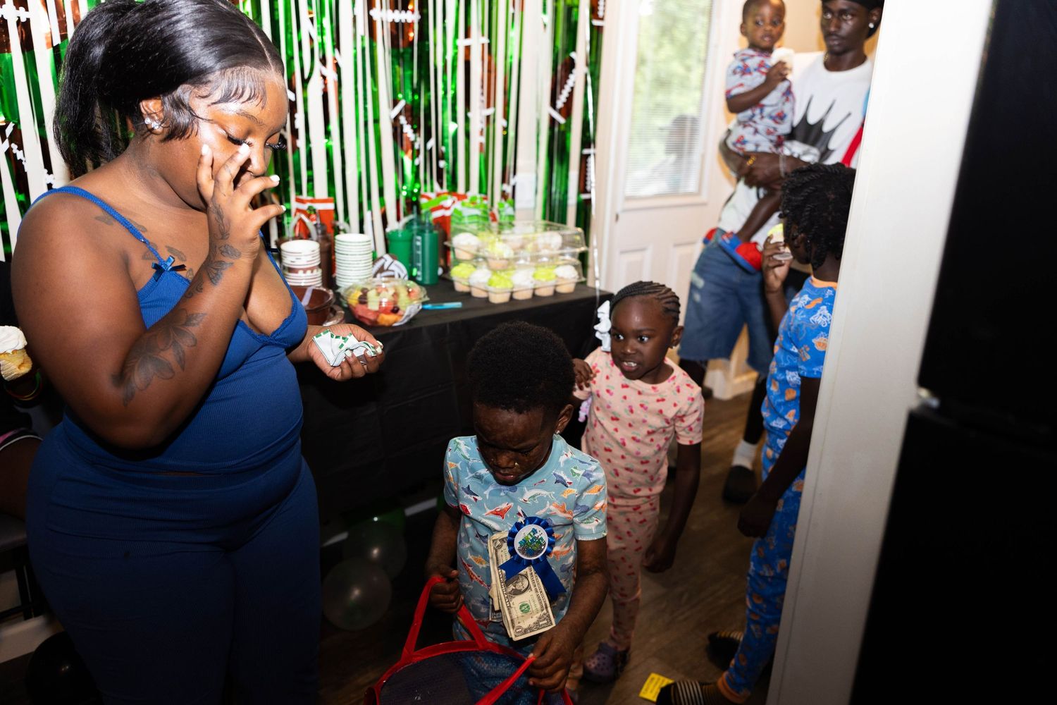 A woman on the phone at a colorful birthday party with children gathered around in a decorated room.