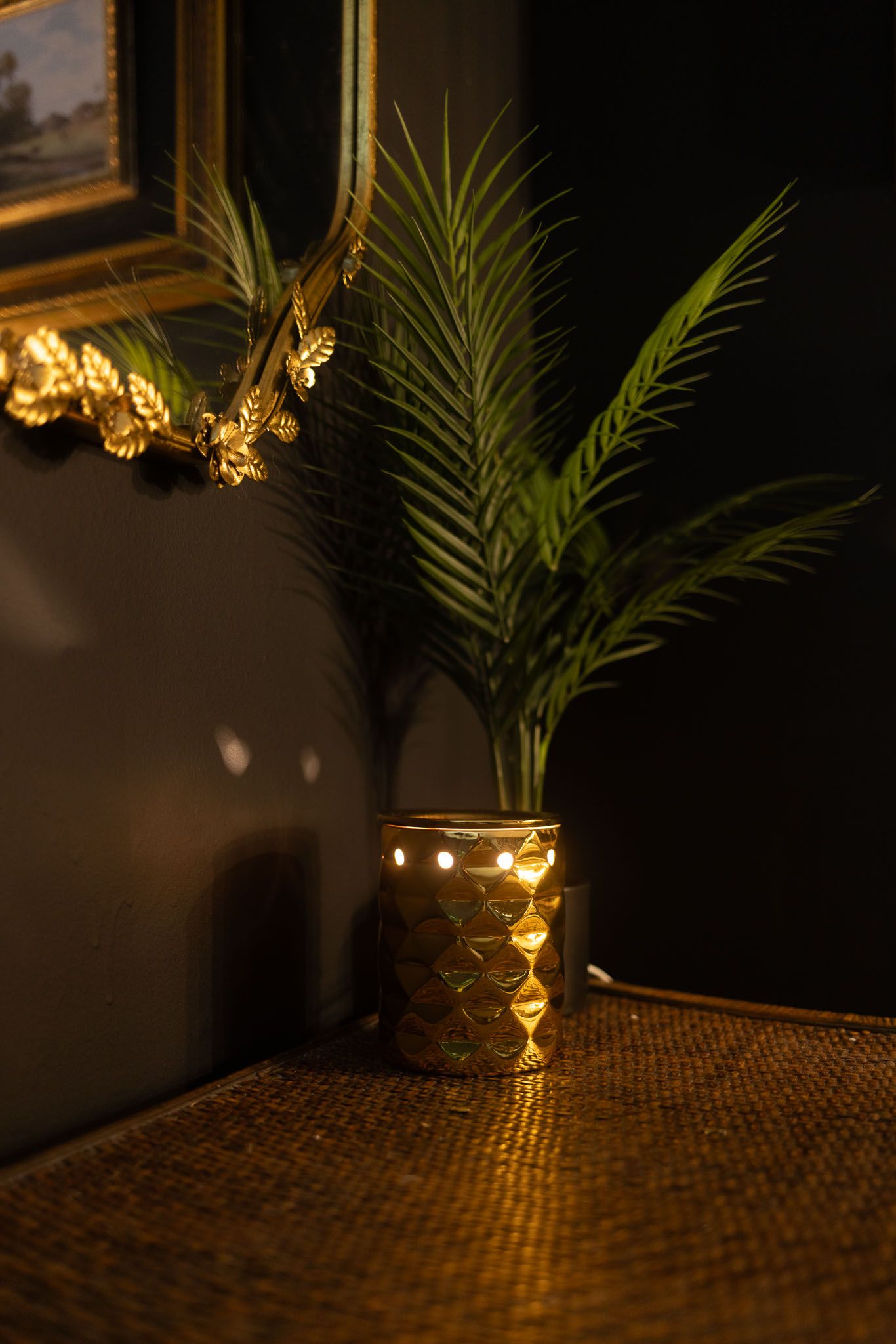 A martini glass sits on a textured surface with palm fronds and warm lighting creating a moody tropical ambiance.