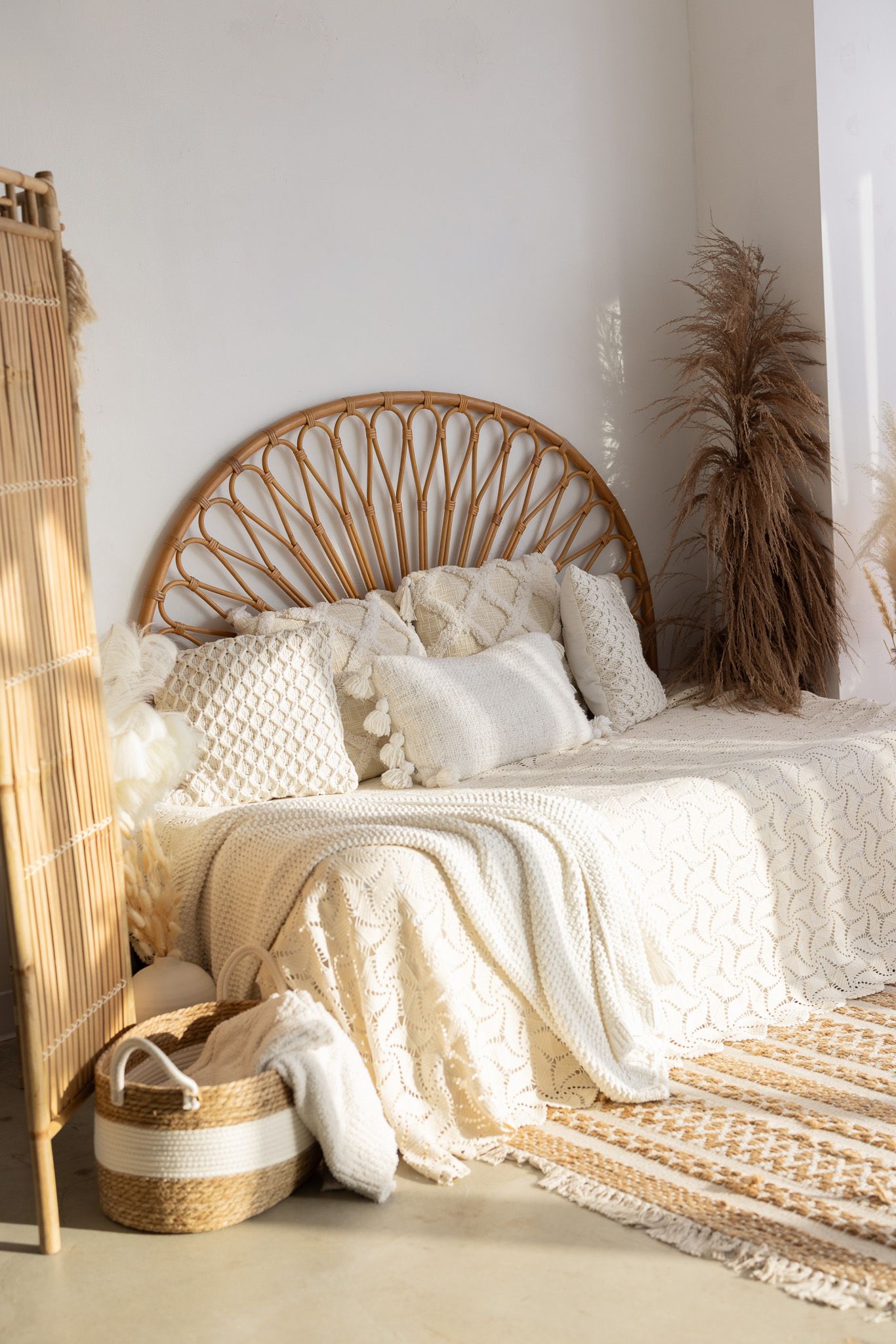 Boho bedroom with rattan headboard, white knit bedding, woven basket, pampas grass, and natural textures in neutral tones.