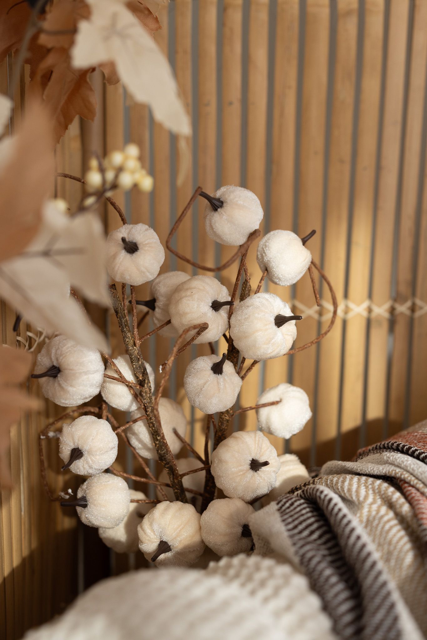 White decorative mini pumpkins on branches arranged in a fall autumn vignette with warm neutral tones.