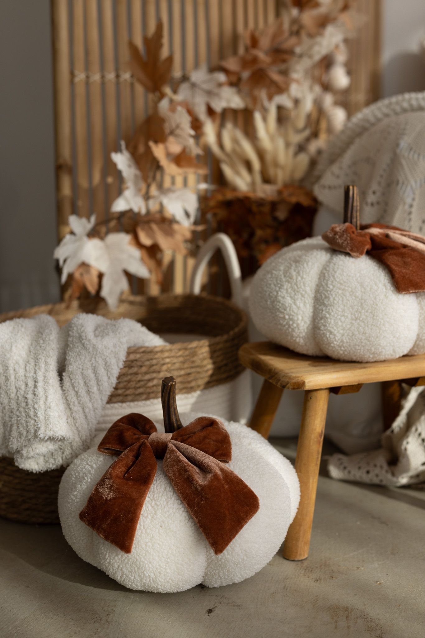 White boucle pumpkins with brown velvet bows and stem, styled with dried leaves and wicker basket for fall decor.