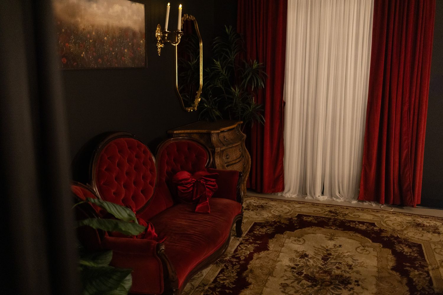Elegant red velvet armchair beside a ornate dresser with gold candelabra, framed by rich crimson curtains and a vintage rug.