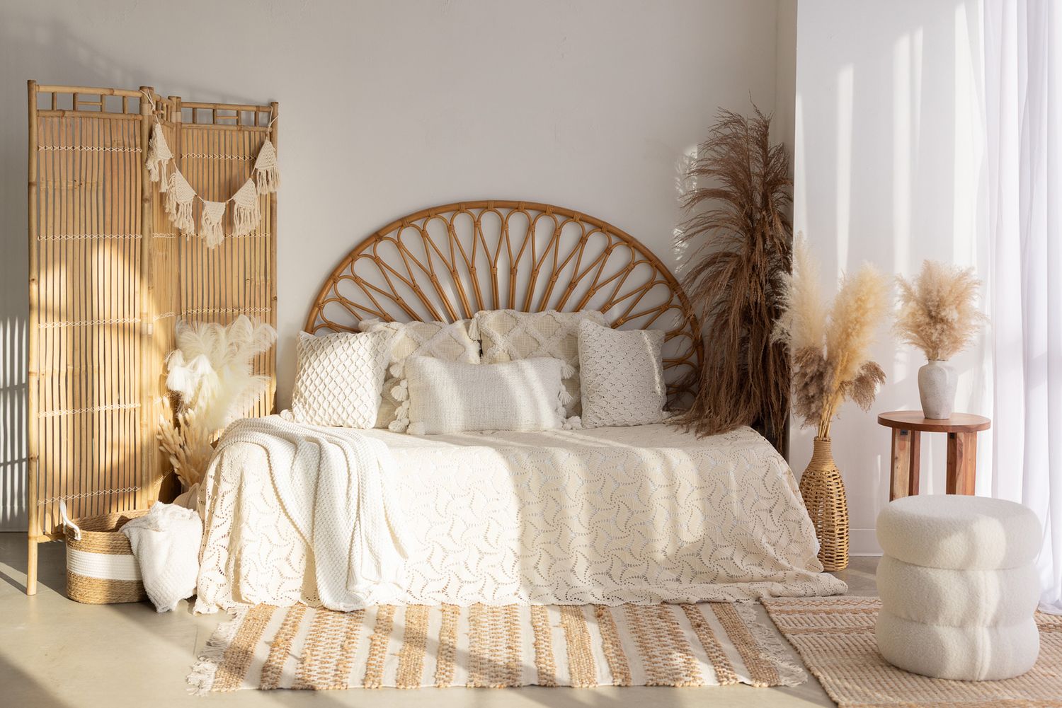 Boho bedroom with rattan headboard, white bedding, pampas grass, macrame wall decor, and warm natural light.