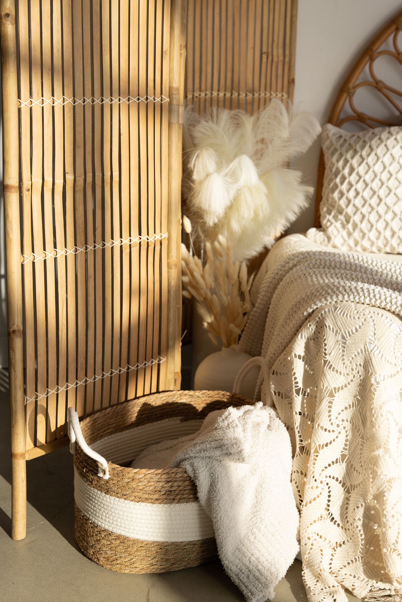 Boho bedroom corner with rattan screen, wicker basket, knit throw blanket, and dried pampas grass decor.