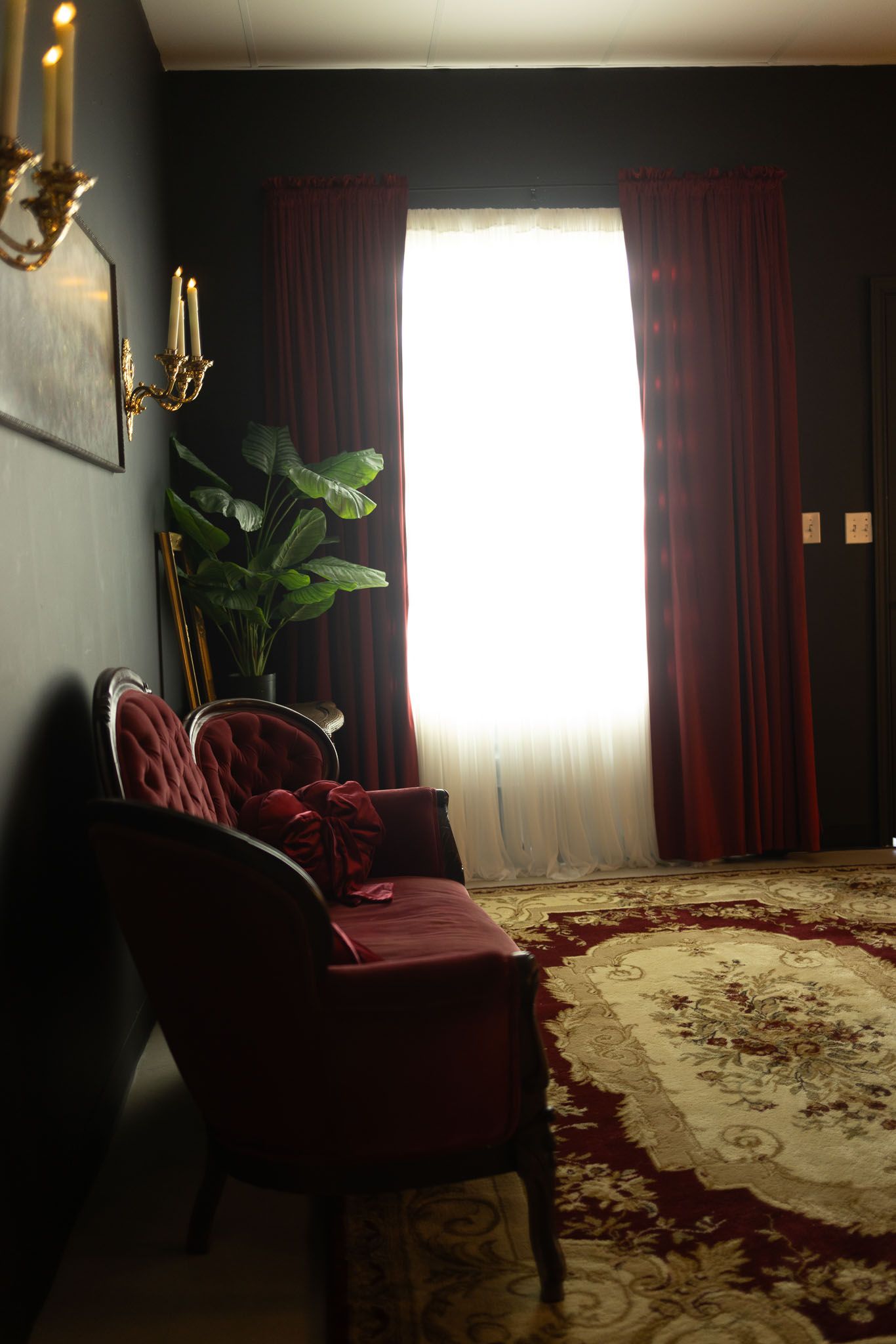 Elegant living room interior with burgundy armchair, patterned area rug, and dramatic window lighting.