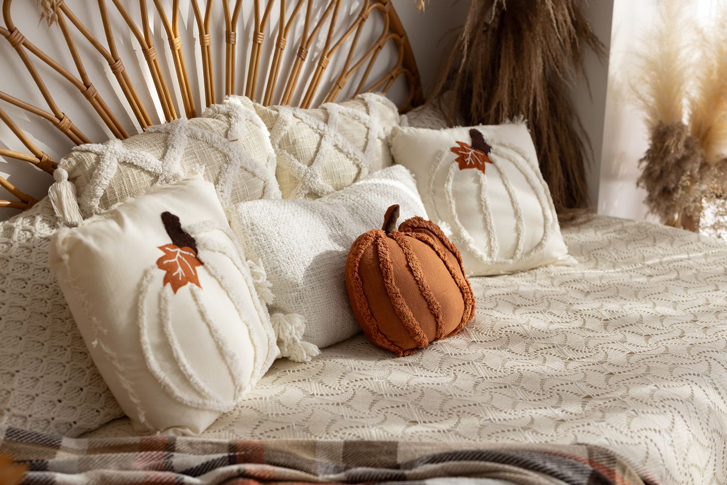 Cozy fall bedroom with cream knit pillows and pumpkin-shaped cushions in white and rust orange on a textured white bedspread.