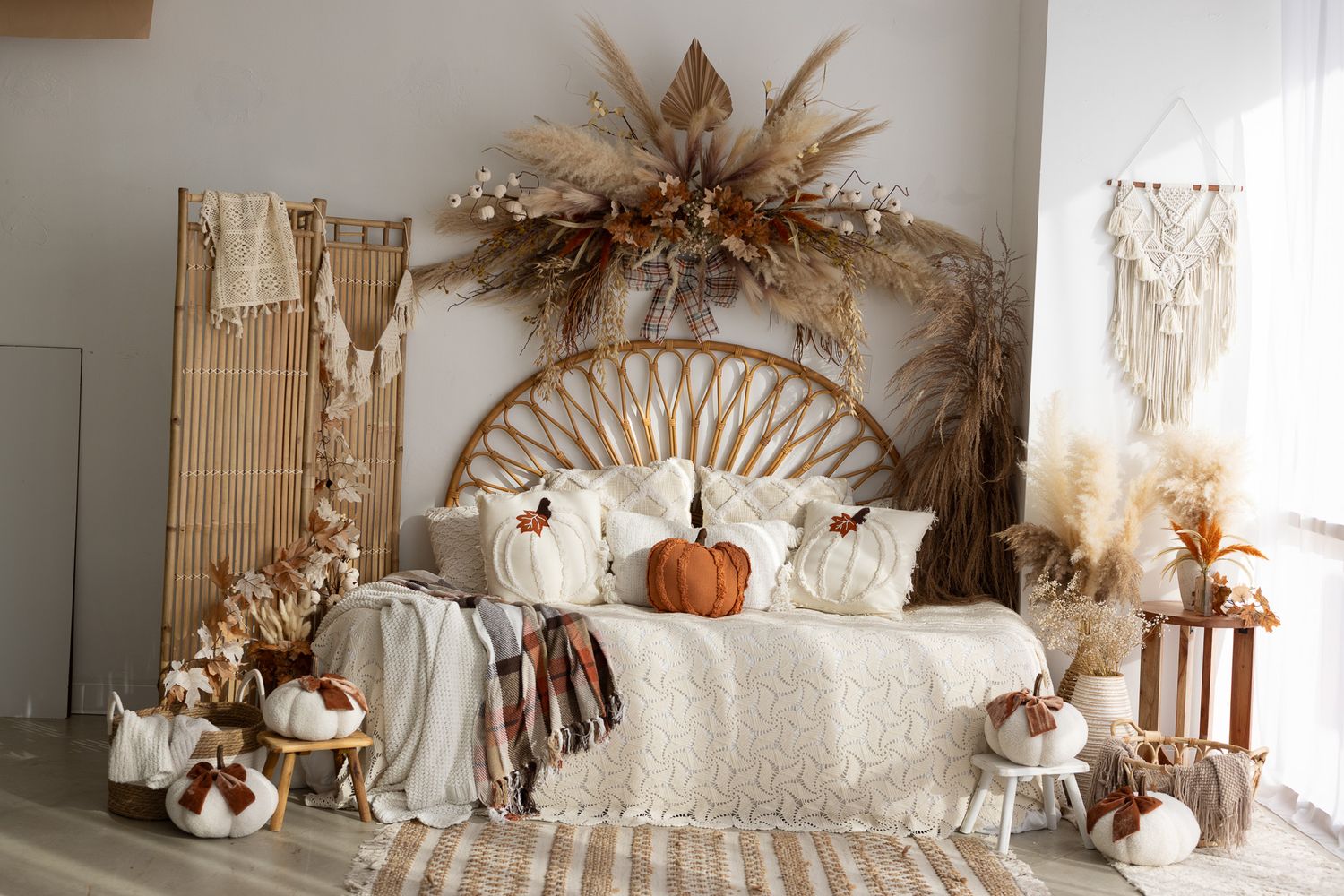 Boho bedroom with rattan headboard, dried floral arrangement, pumpkins, and neutral fall decor in white and earthy tones.