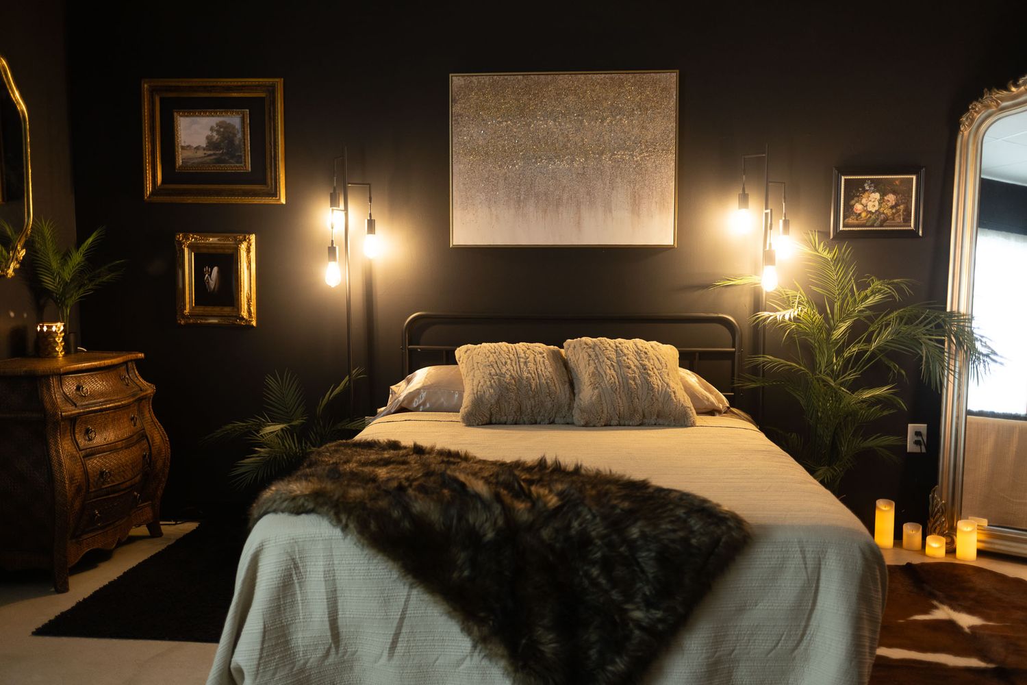 Luxurious dark bedroom featuring gold accents, pendant lights, and tropical plants against black walls.