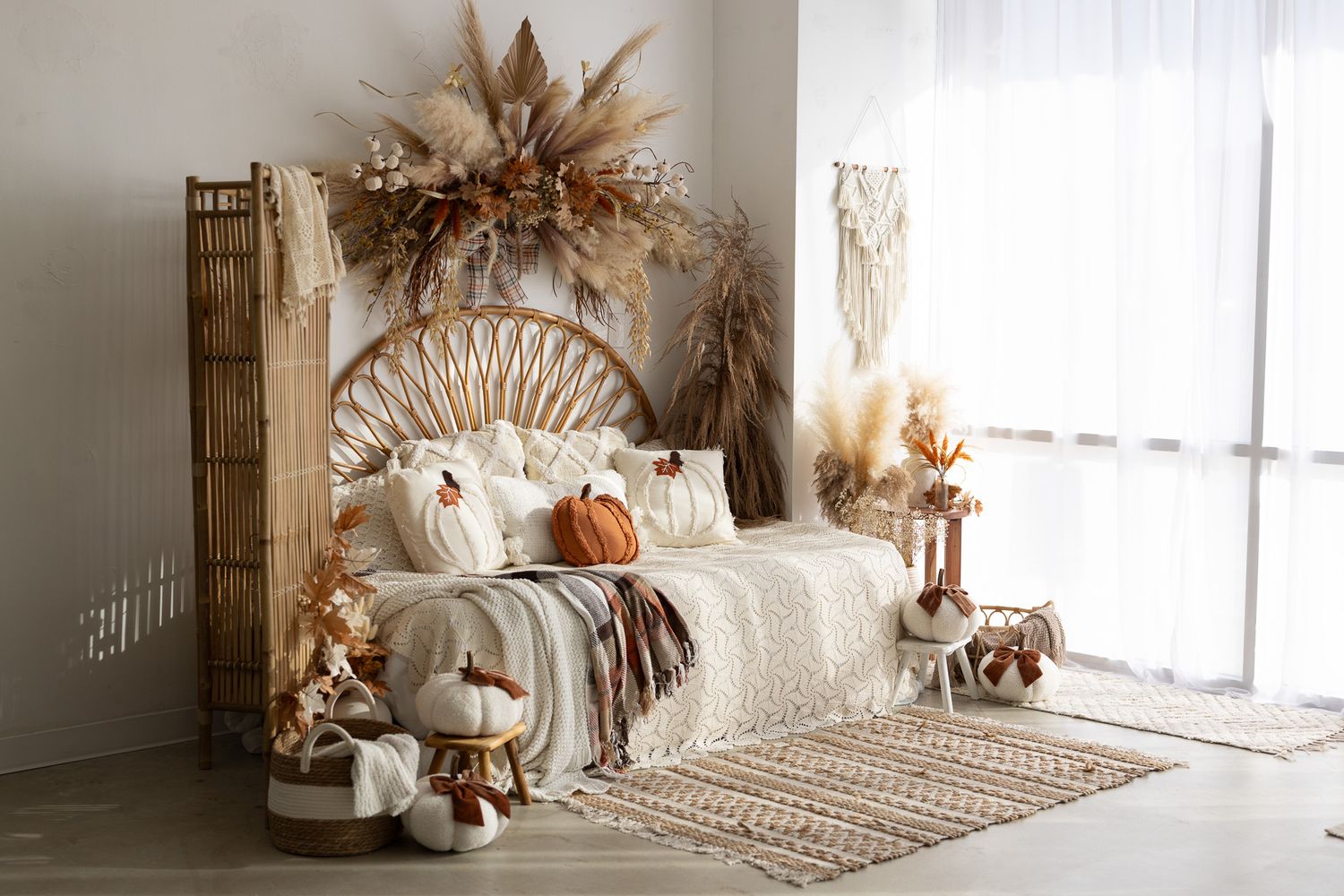 Boho bedroom with rattan headboard, macrame decor, pampas grass, and autumn pumpkins in warm neutral tones.
