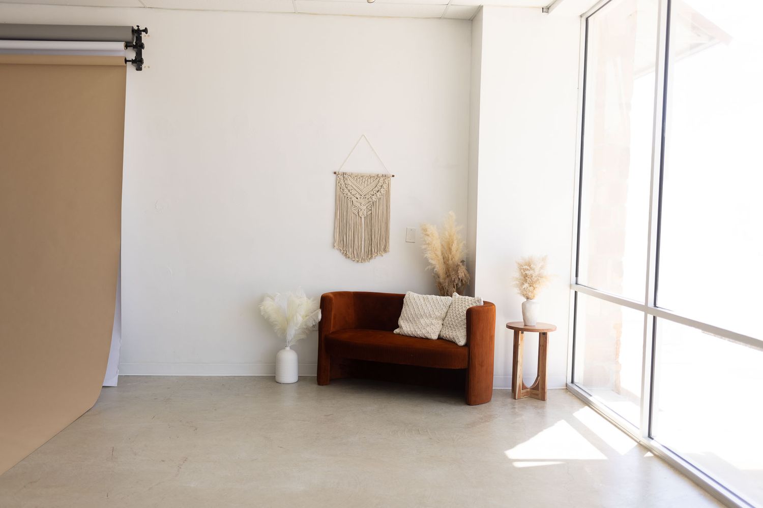 Bright, minimalist interior space with white walls, large windows, and a macrame wall hanging in natural light.