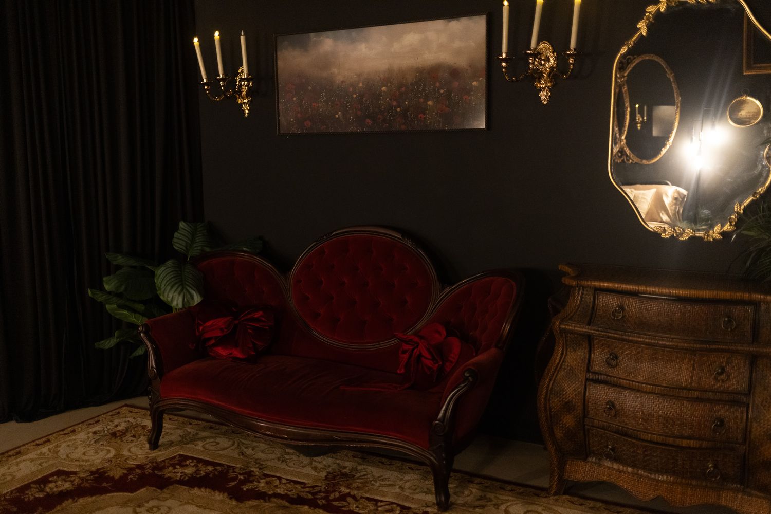 Elegant Victorian sitting room with red velvet chaise lounge, ornate mirror, candle sconces, and dark moody decor.