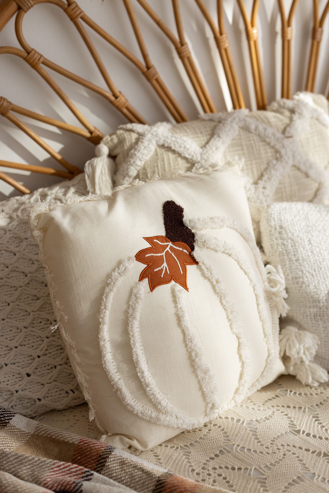 Cream boho throw pillow with pumpkin design and fall leaf applique on rattan chair with cozy blanket.
