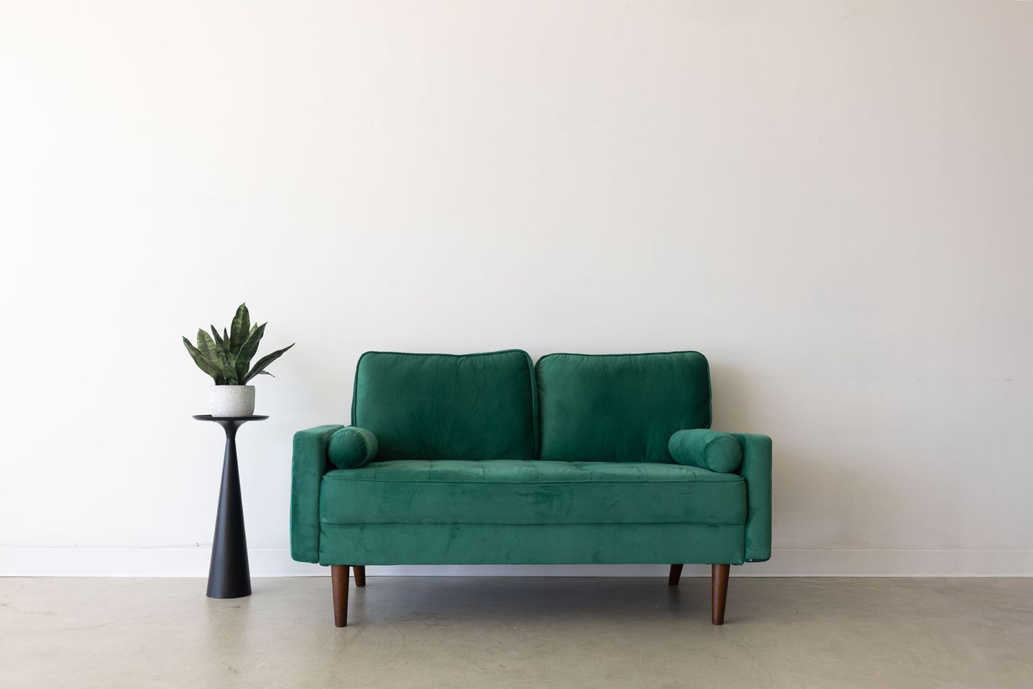 A modern emerald green velvet sofa with wooden legs is shown from multiple angles against a white wall.