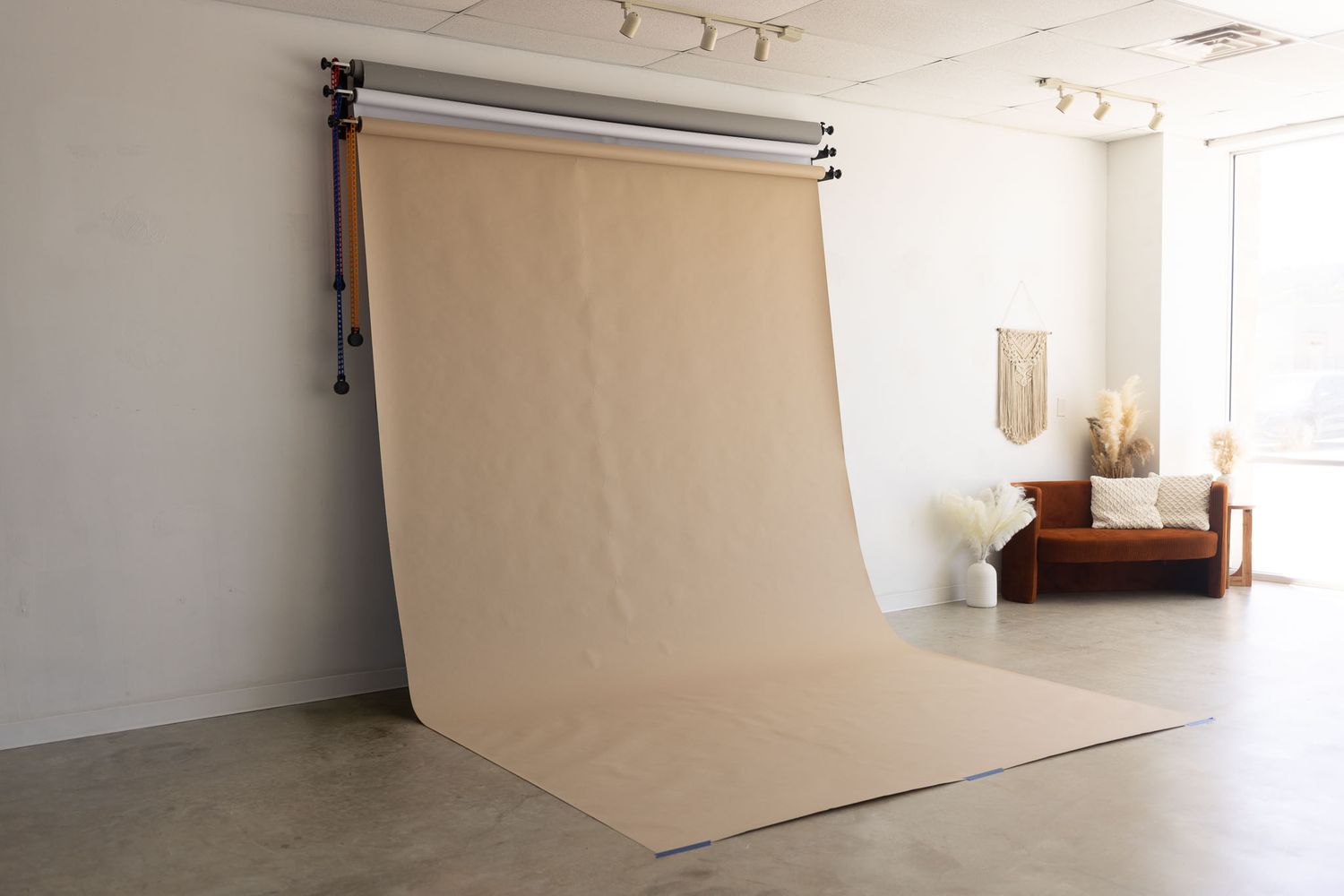 Professional photography studio interior with seamless beige backdrop, track lighting, and natural window light.