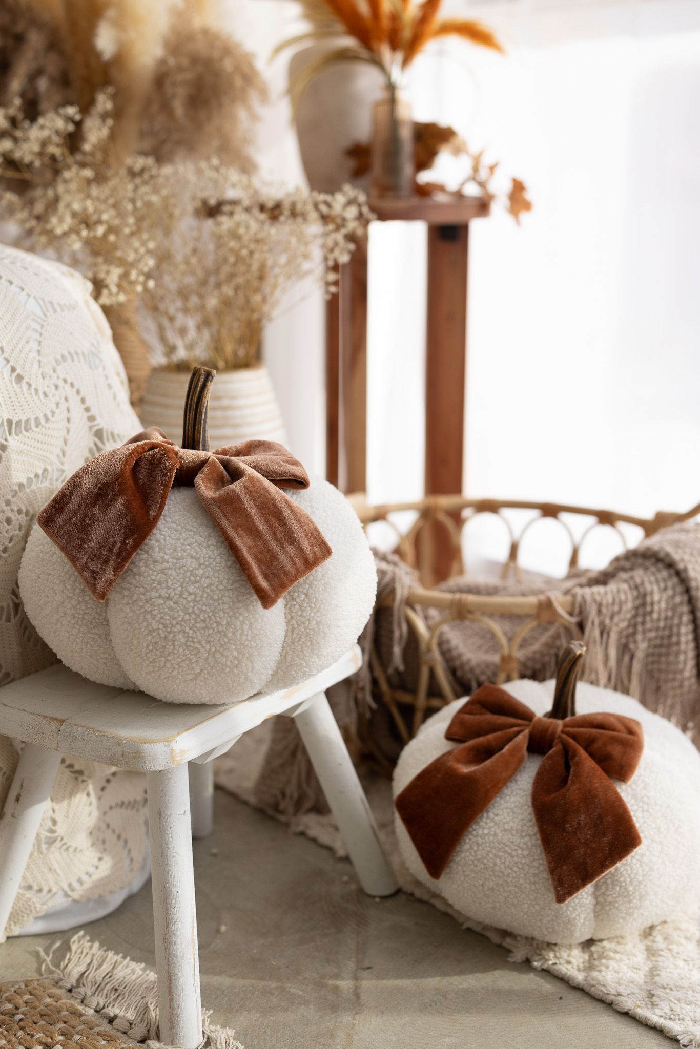 Two white fluffy decorative pumpkins with brown velvet bows displayed in a cozy boho fall home decor setting.