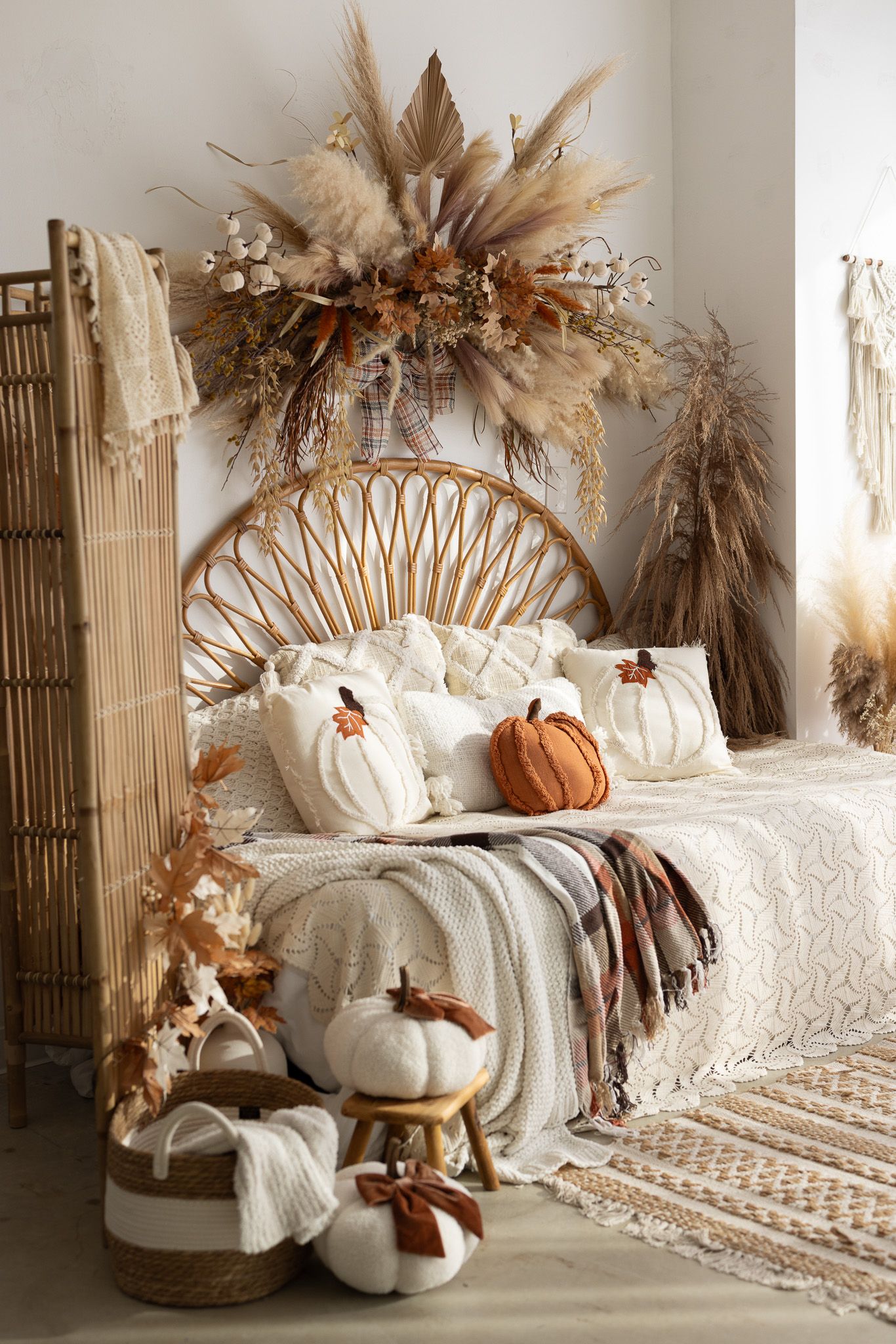 Boho bedroom with rattan headboard, pumpkin pillows, dried pampas grass, and warm autumn decor in neutral tones.