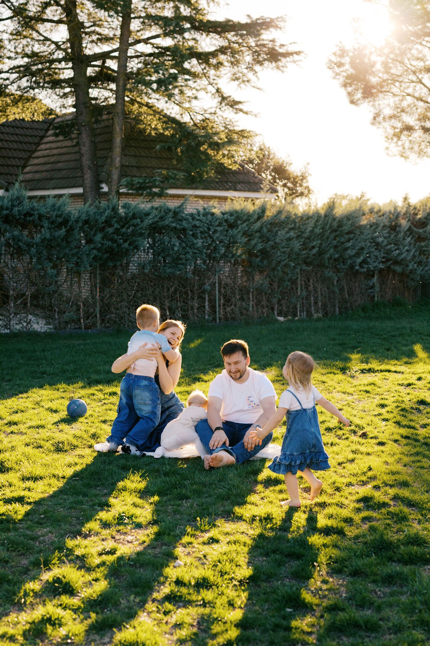 Happy family with children enjoying a sunny day together on green grass in a garden.