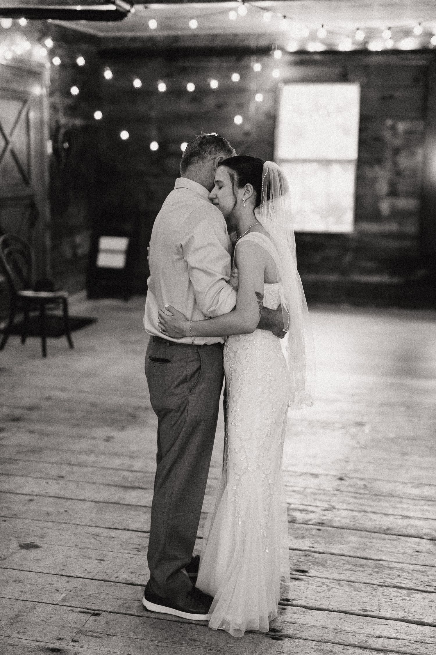 Black and white photo of bride and her father sharing emotions during their dance in the 1774 Inn with string lights in the background.