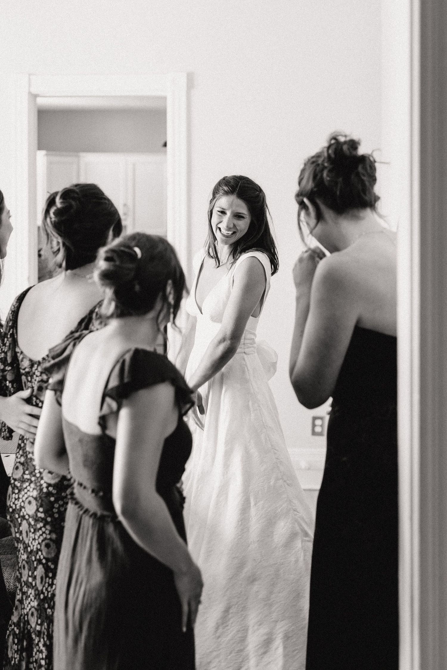 A sequence of black and white photos showing a bridal party getting ready in a room with white walls.