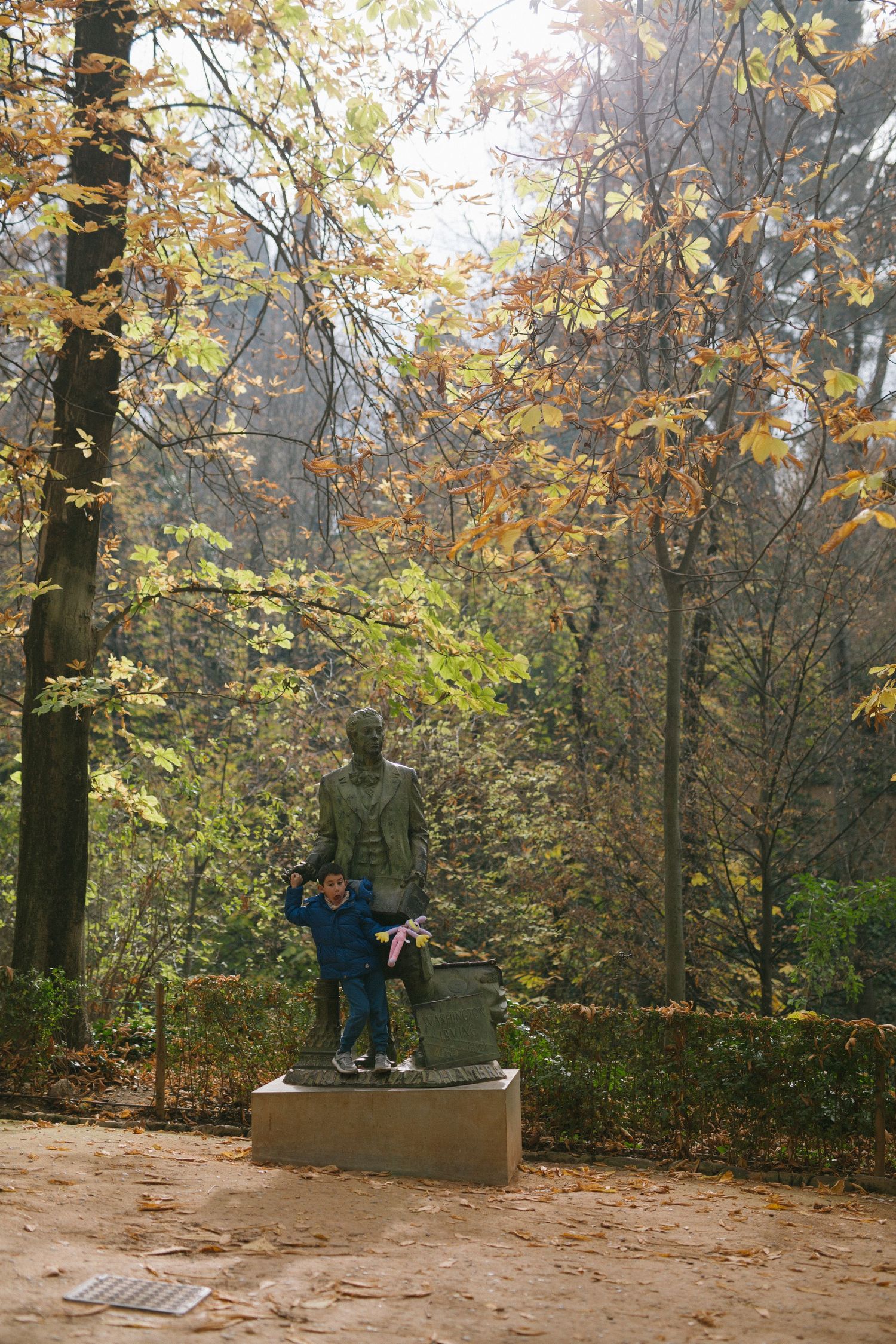Bronze statue surrounded by colorful autumn foliage in a park setting.