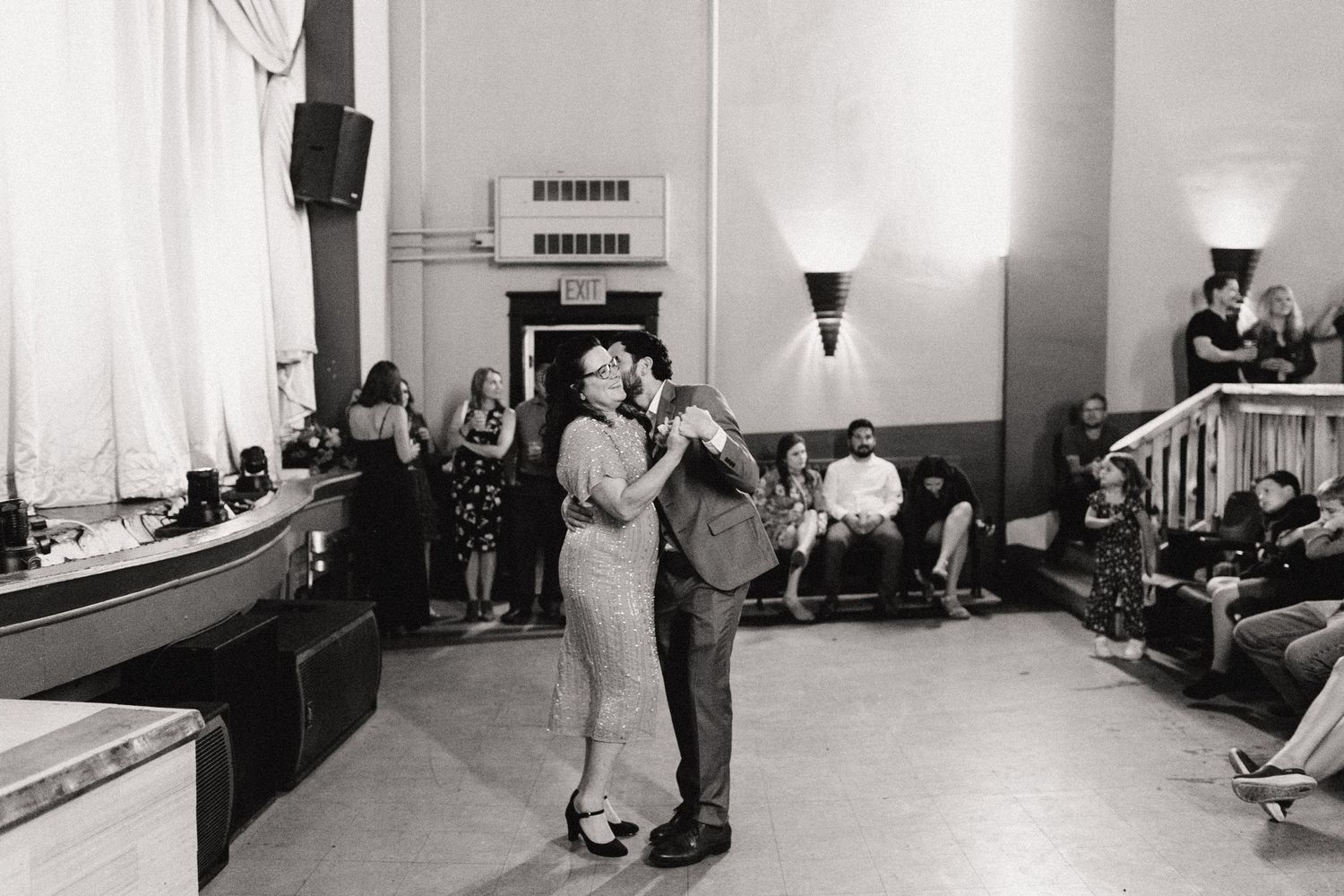 A black and white vintage photo shows two people dancing in what appears to be a casual indoor gathering space.