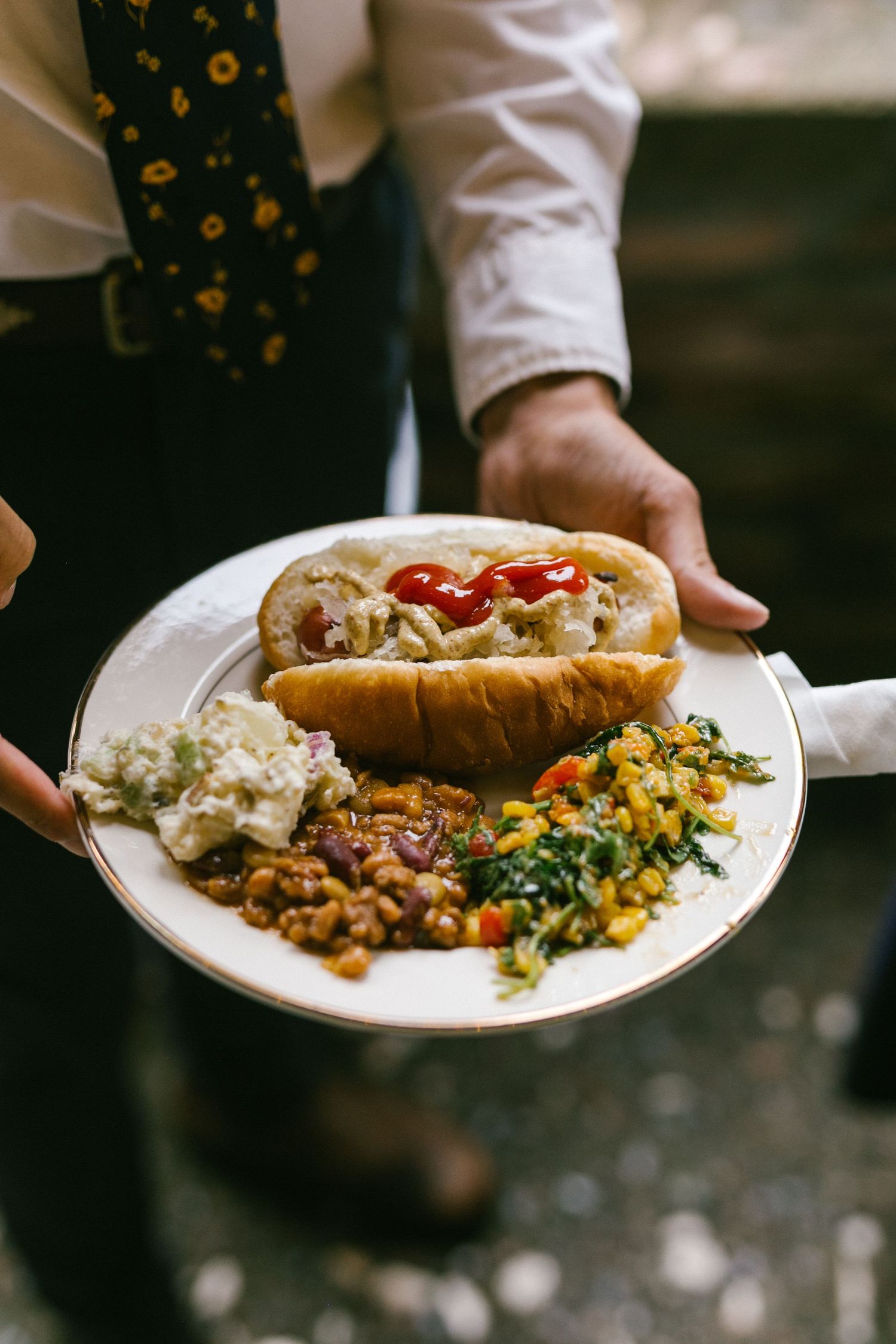A plate of colorful wedding reception food featuring a sandwich, sides, and garnishes.