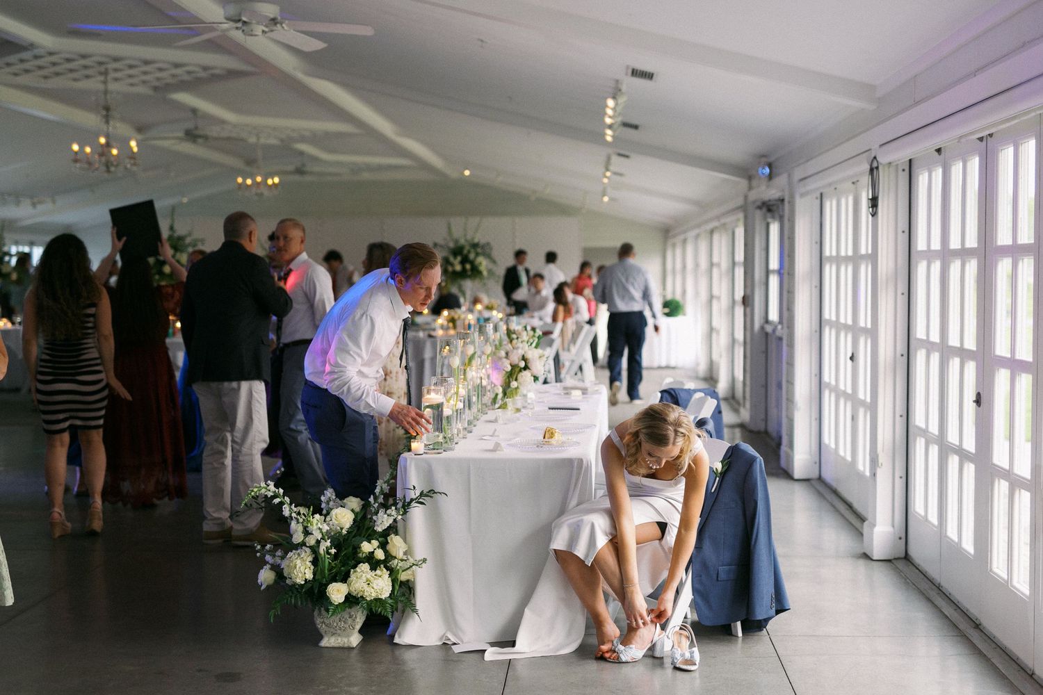 Panoramic view of a bright indoor venue with white tables set for a wedding reception and large windows along the wall.