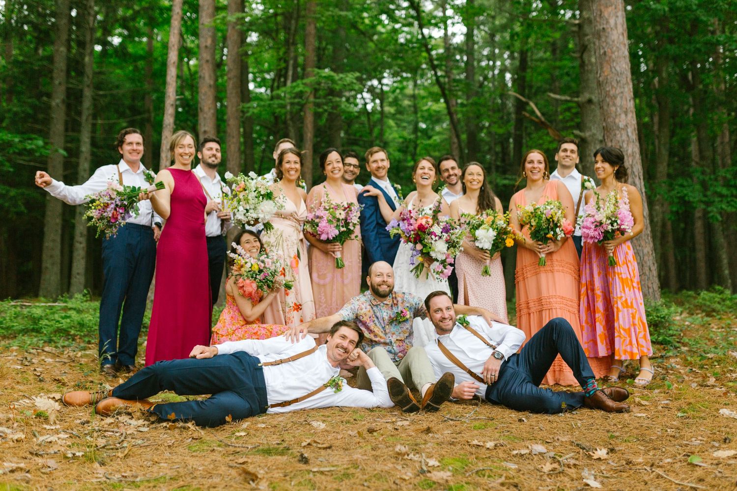 A wedding party wearing colorful gowns and suits poses together in a scenic forest setting.