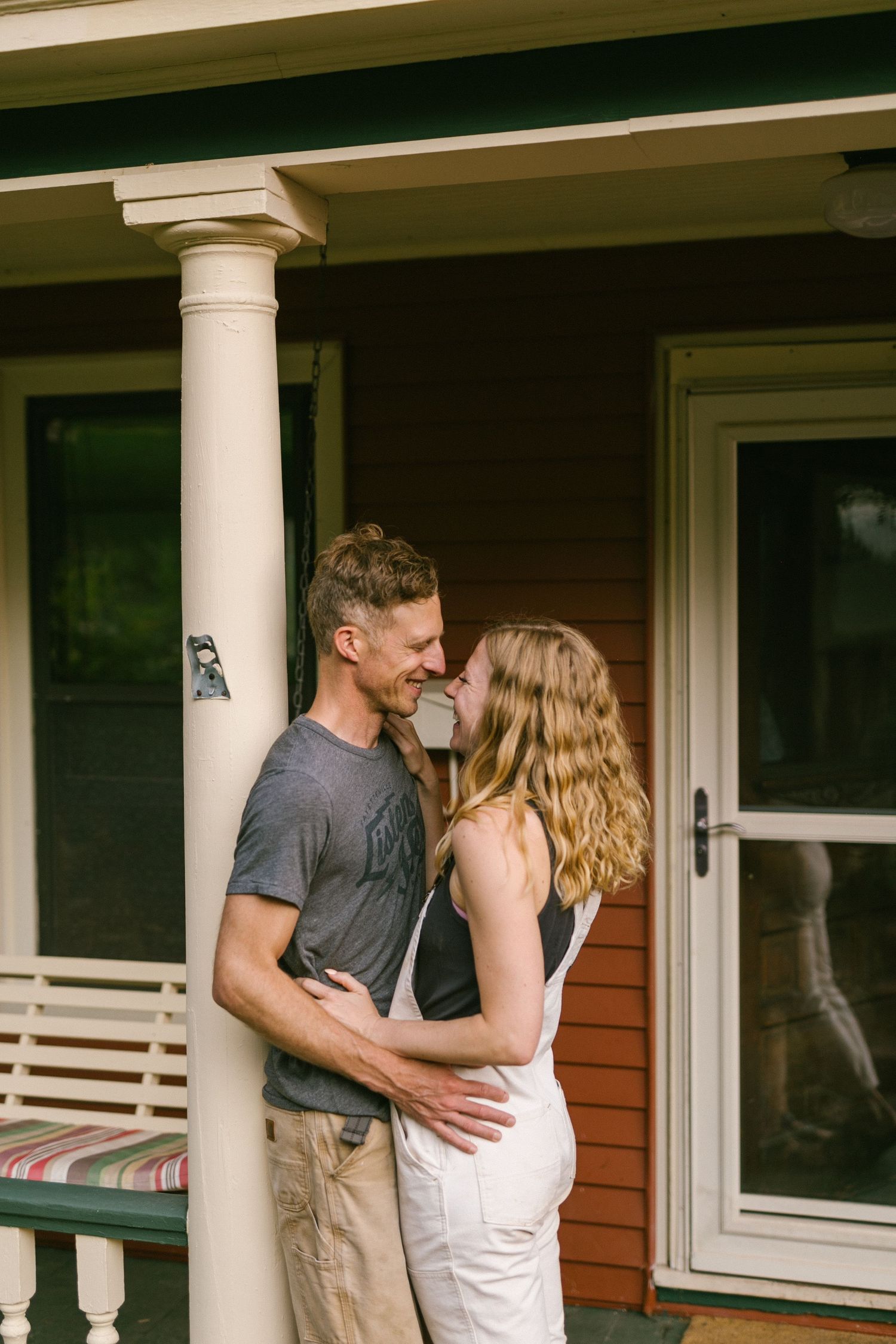 Romantic couple moment on a front porch with white columns and rustic charm.