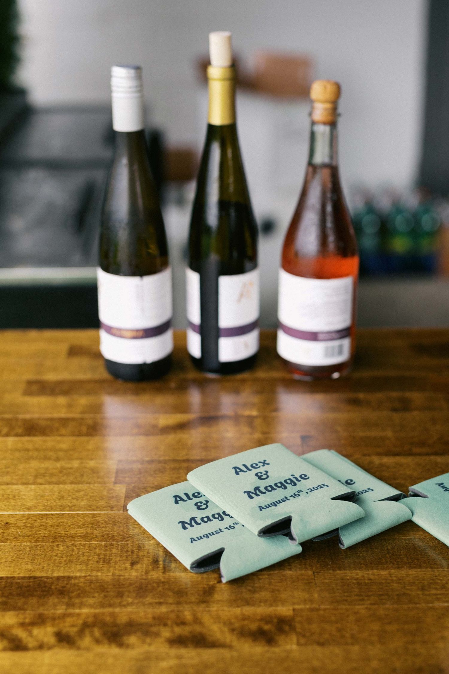 Three wine bottles sit on a wooden table with green paper labels arranged in front of them.