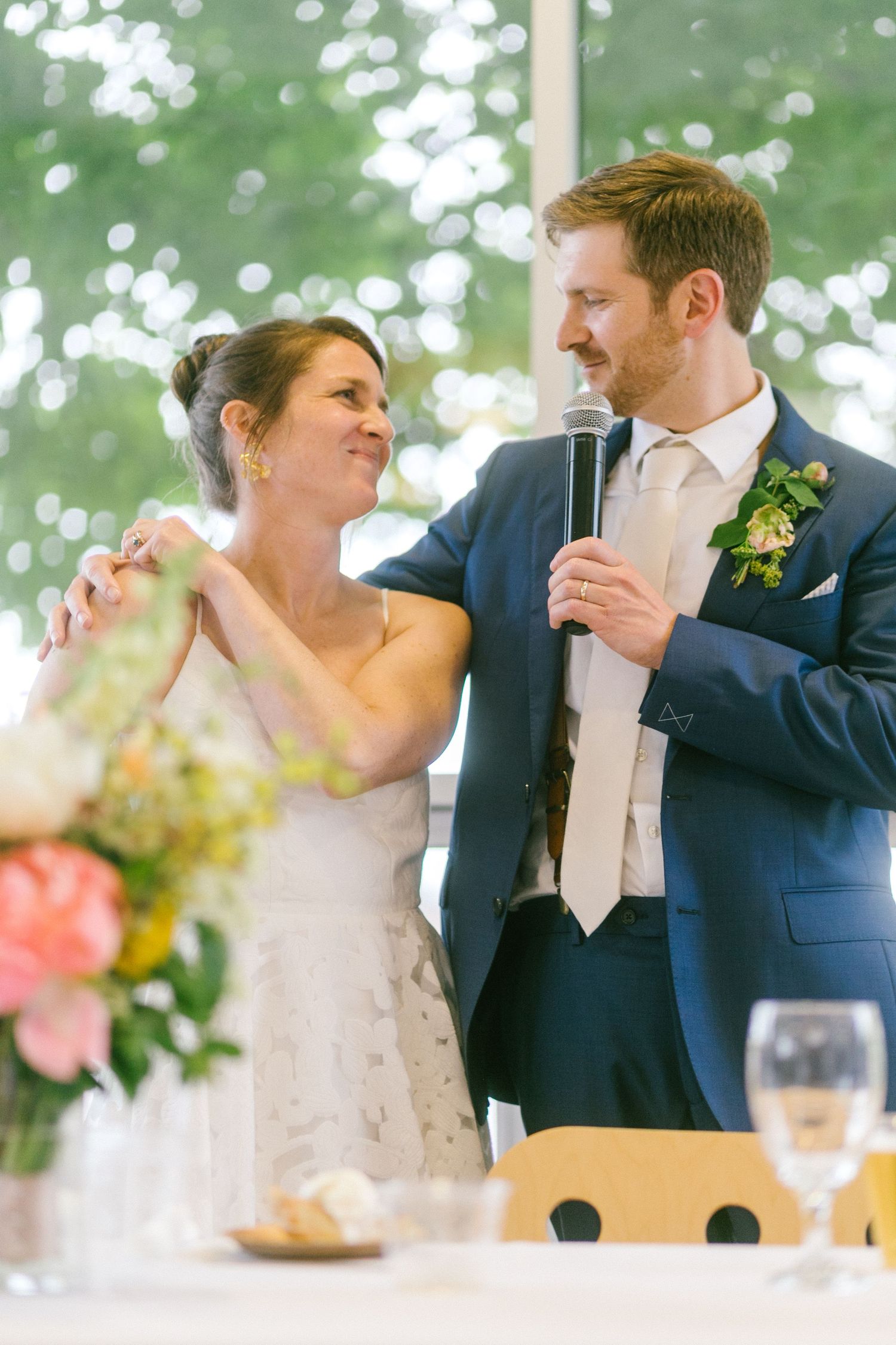 A couple sharing a lighthearted moment while giving toasts at their reception with flowers in foreground.