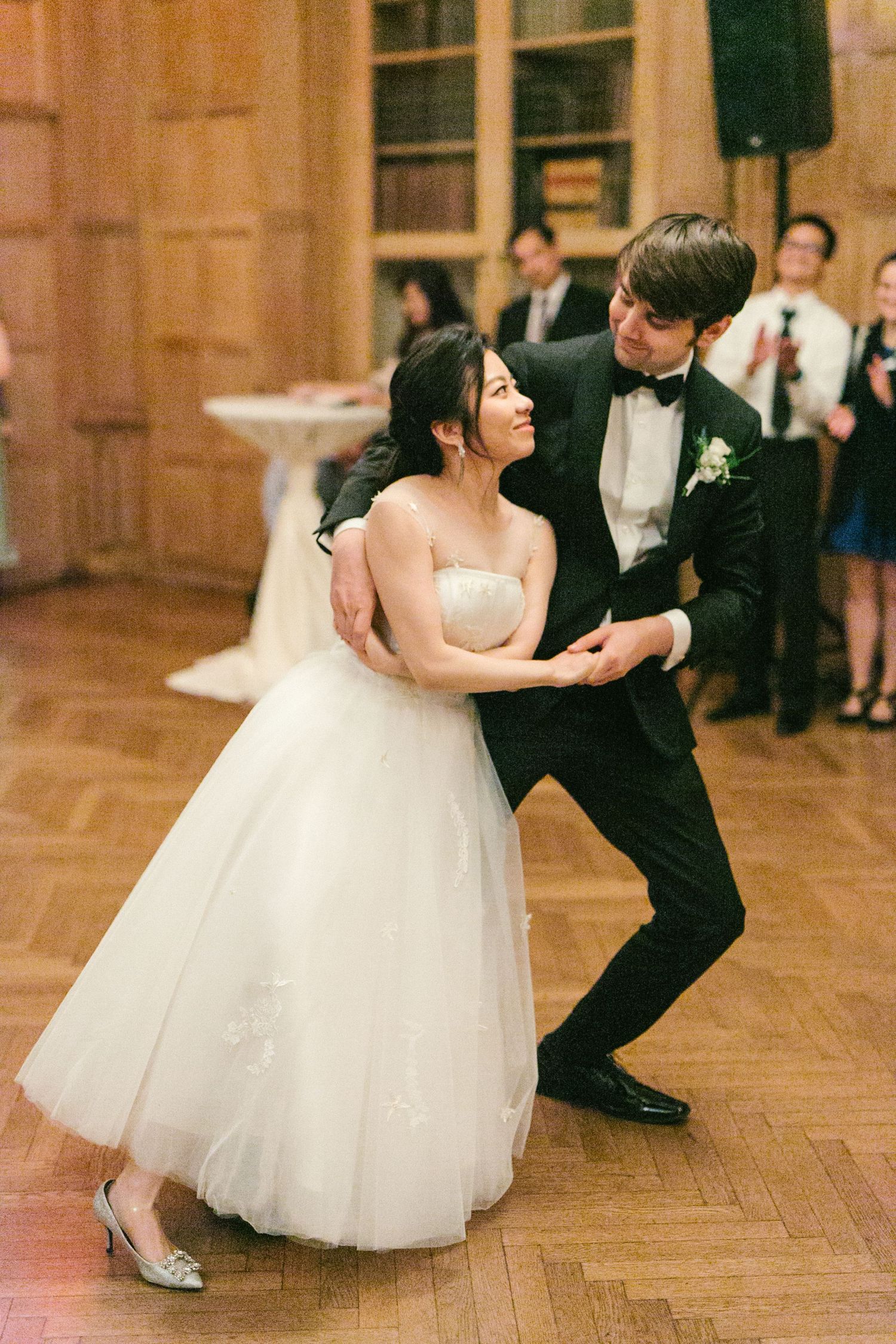 Bride and groom share their first dance in an elegant wood-paneled ballroom during their wedding reception.