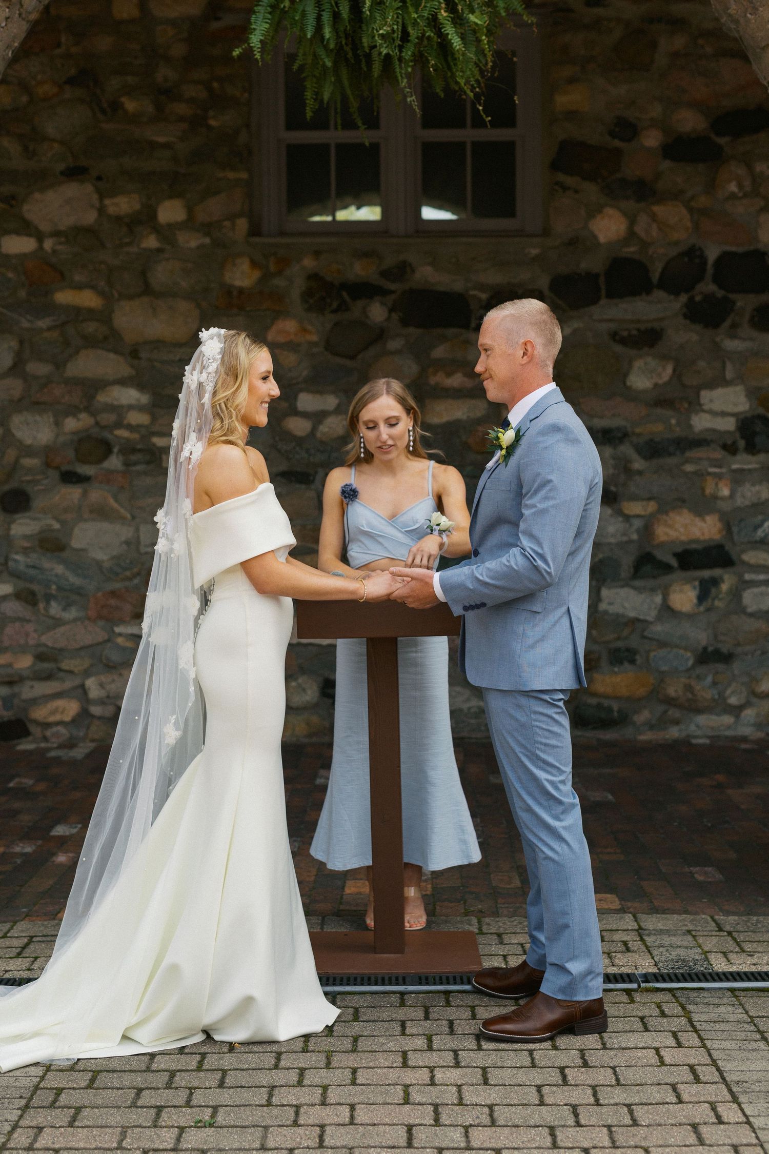 Beautiful wedding ceremony moments captured against a rustic stone wall backdrop with light blue and white attire.