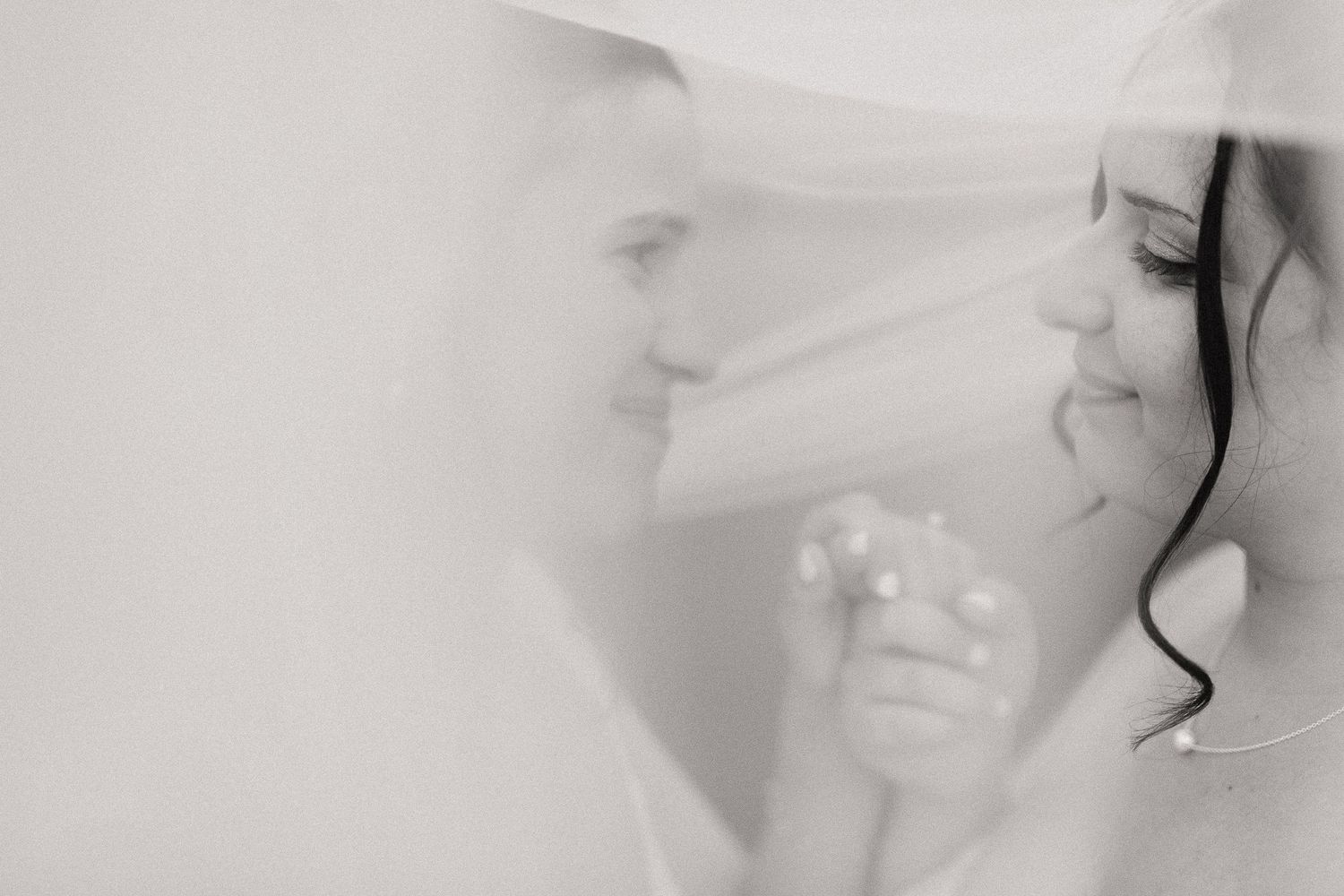 Black and white close-up of couple nearly kissing beneath flowing bridal veil.