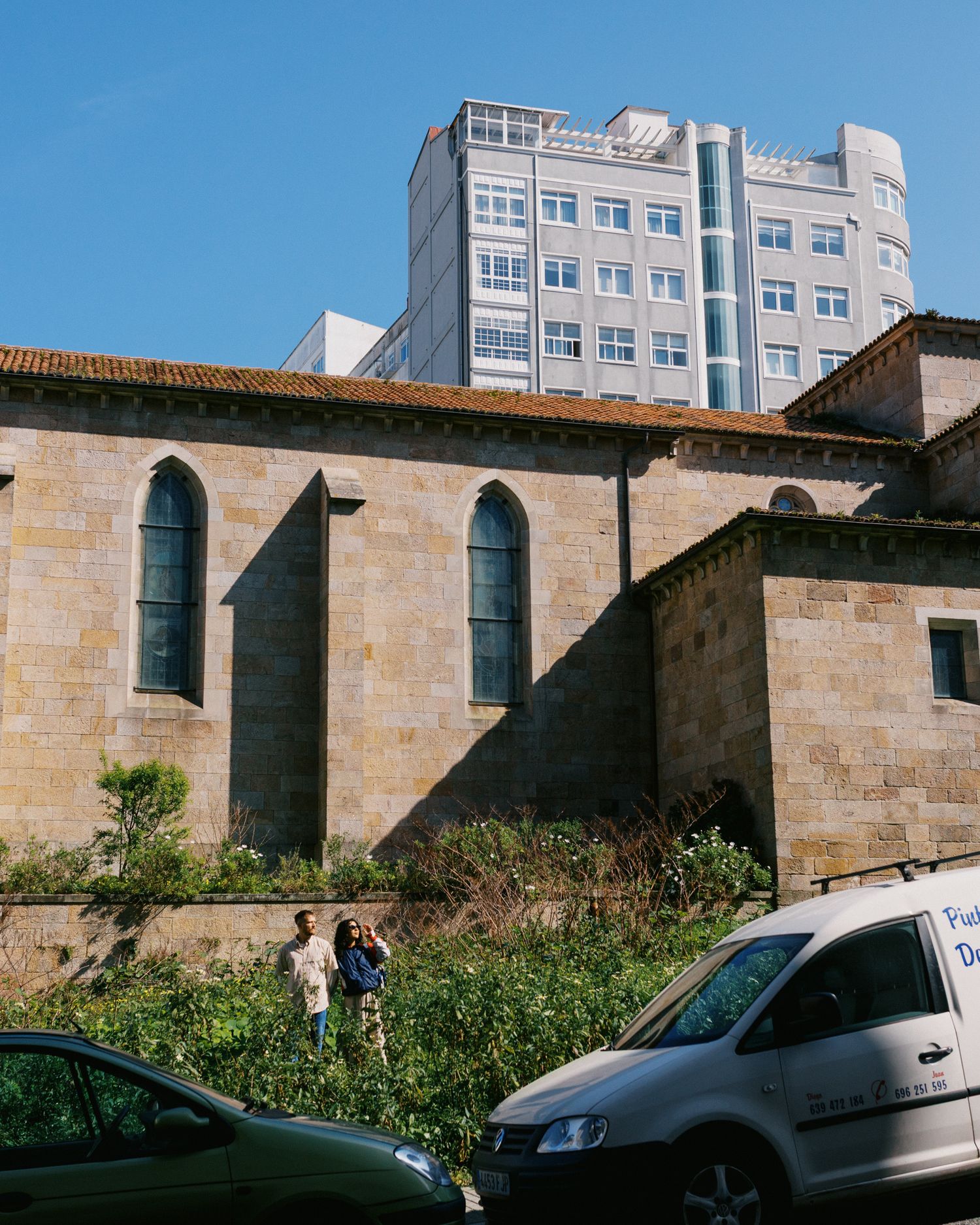 Couple standing near lush greenery beside a historic stone church with gothic arched windows.