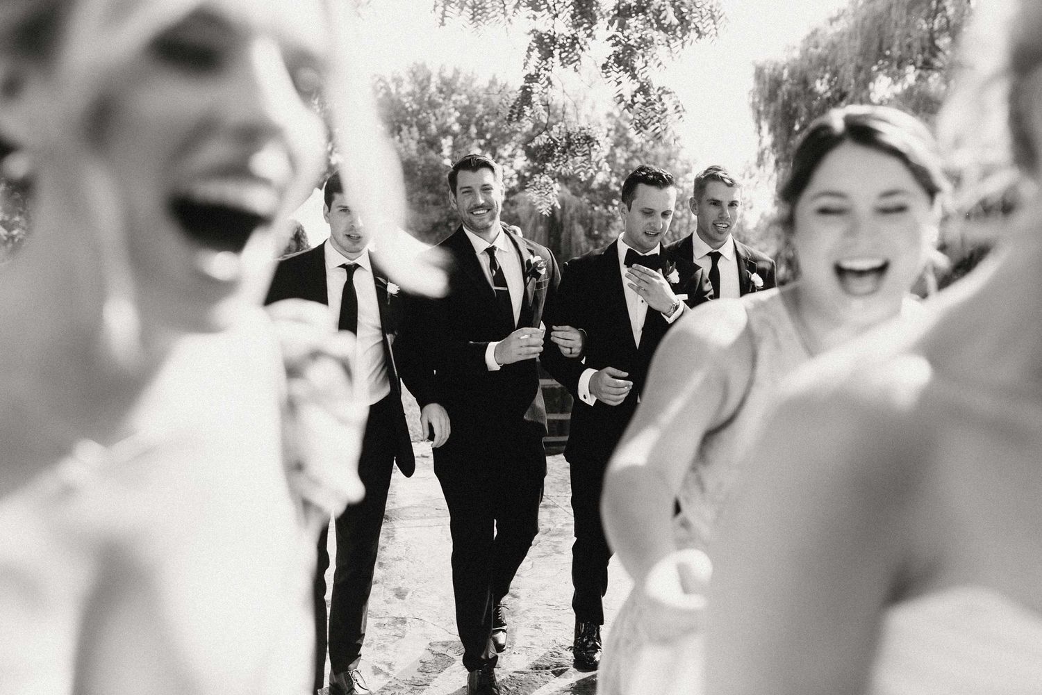 A joyful black and white candid moment captured at an outdoor wedding celebration with people laughing together.