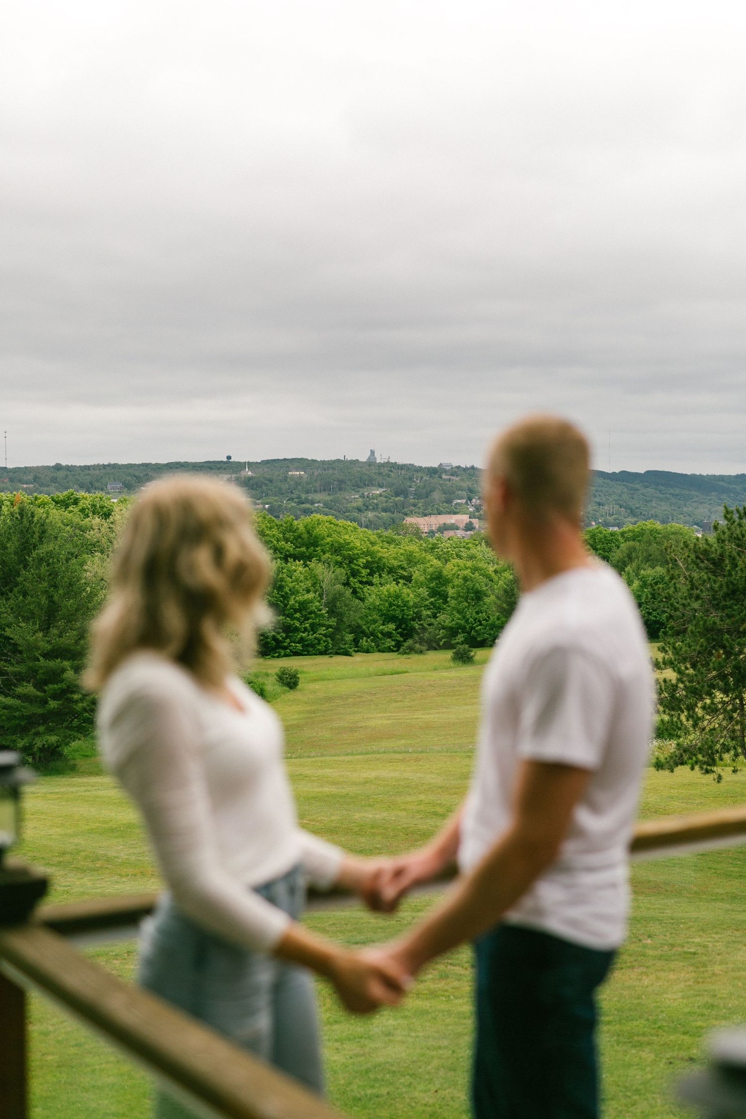 A couple holding hands overlooking a scenic green landscape on an overcast day.
