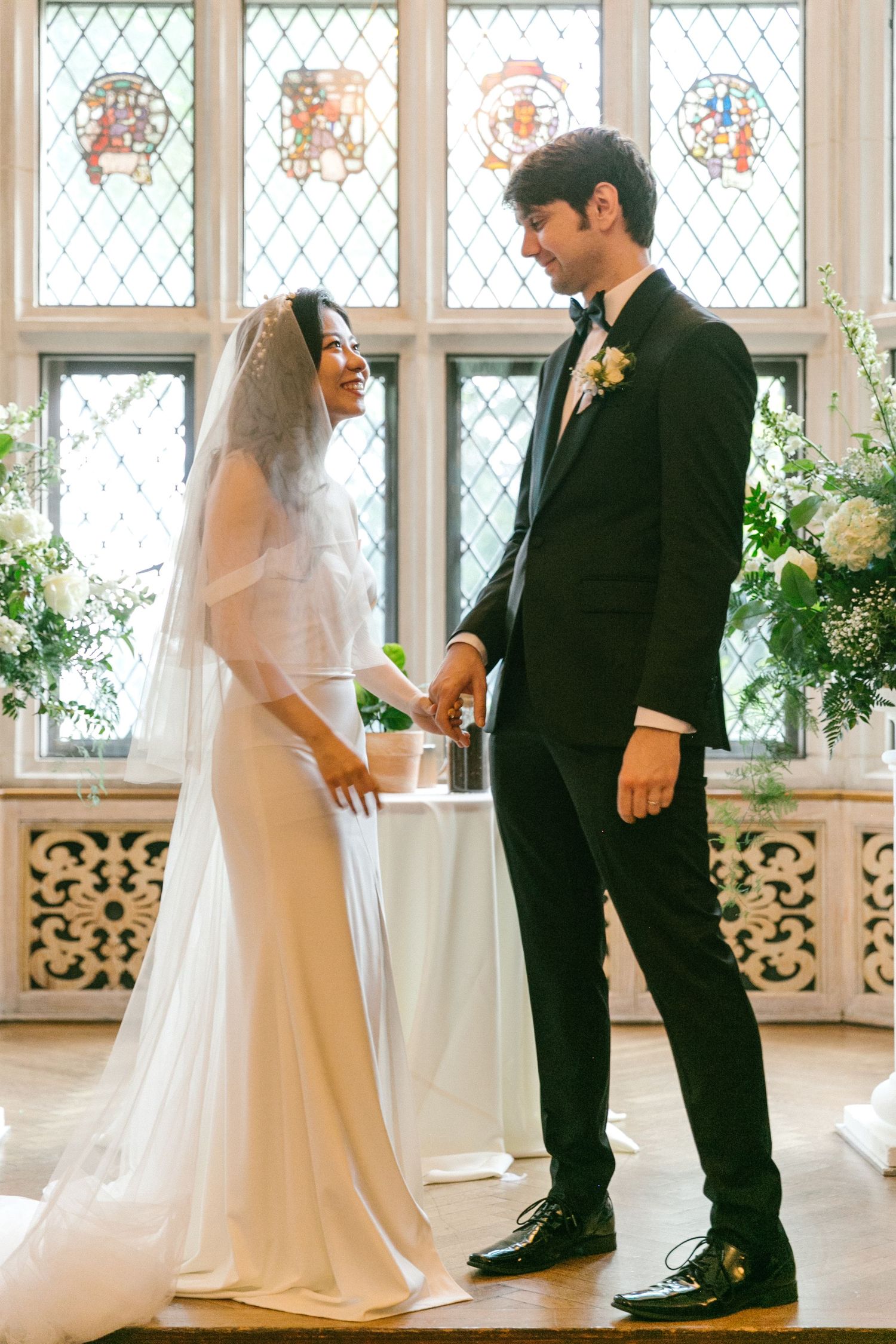 Bride and groom holding hands at the altar with stained glass windows during indoor wedding ceremony.