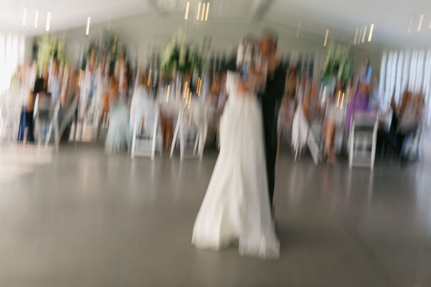 A blurry motion shot of a person in a white wedding dress dancing at a reception.