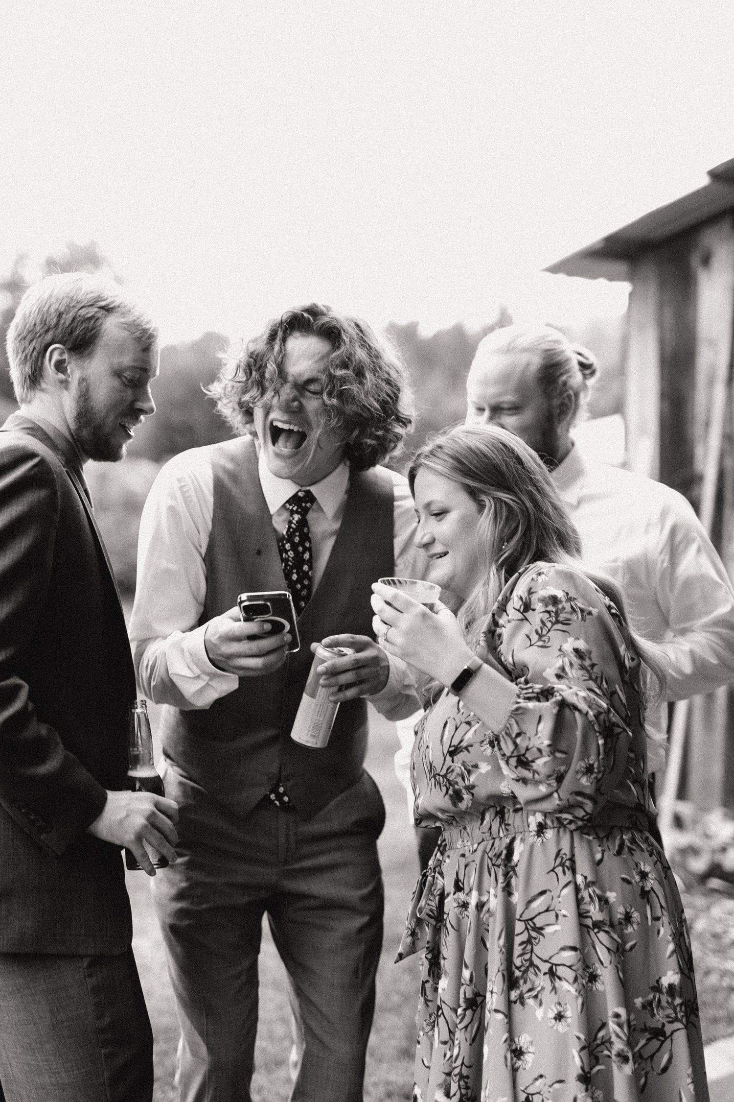 Group laughing while looking at their phones during outdoor wedding reception.
