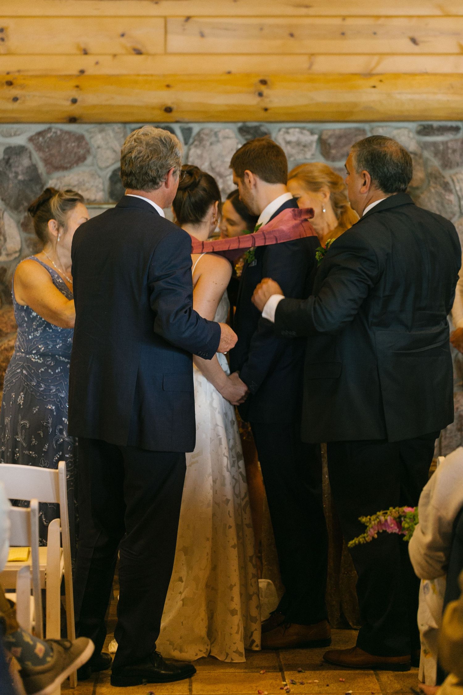 A small group gathers in formal attire during an intimate ceremony in a rustic wood-paneled venue.
