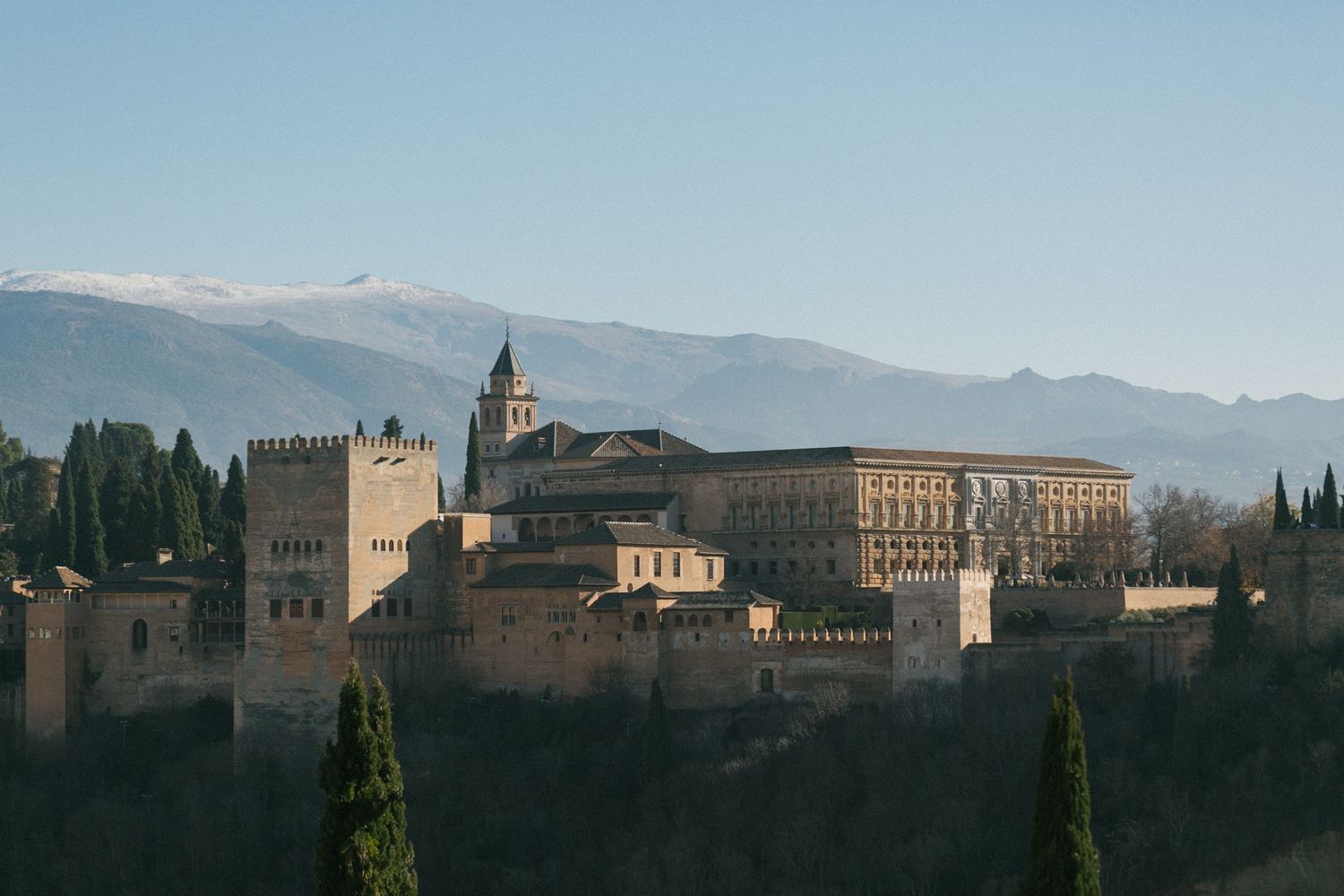 The Alhambra palace complex sits majestically on a hilltop with snow-capped Sierra Nevada mountains in the background.