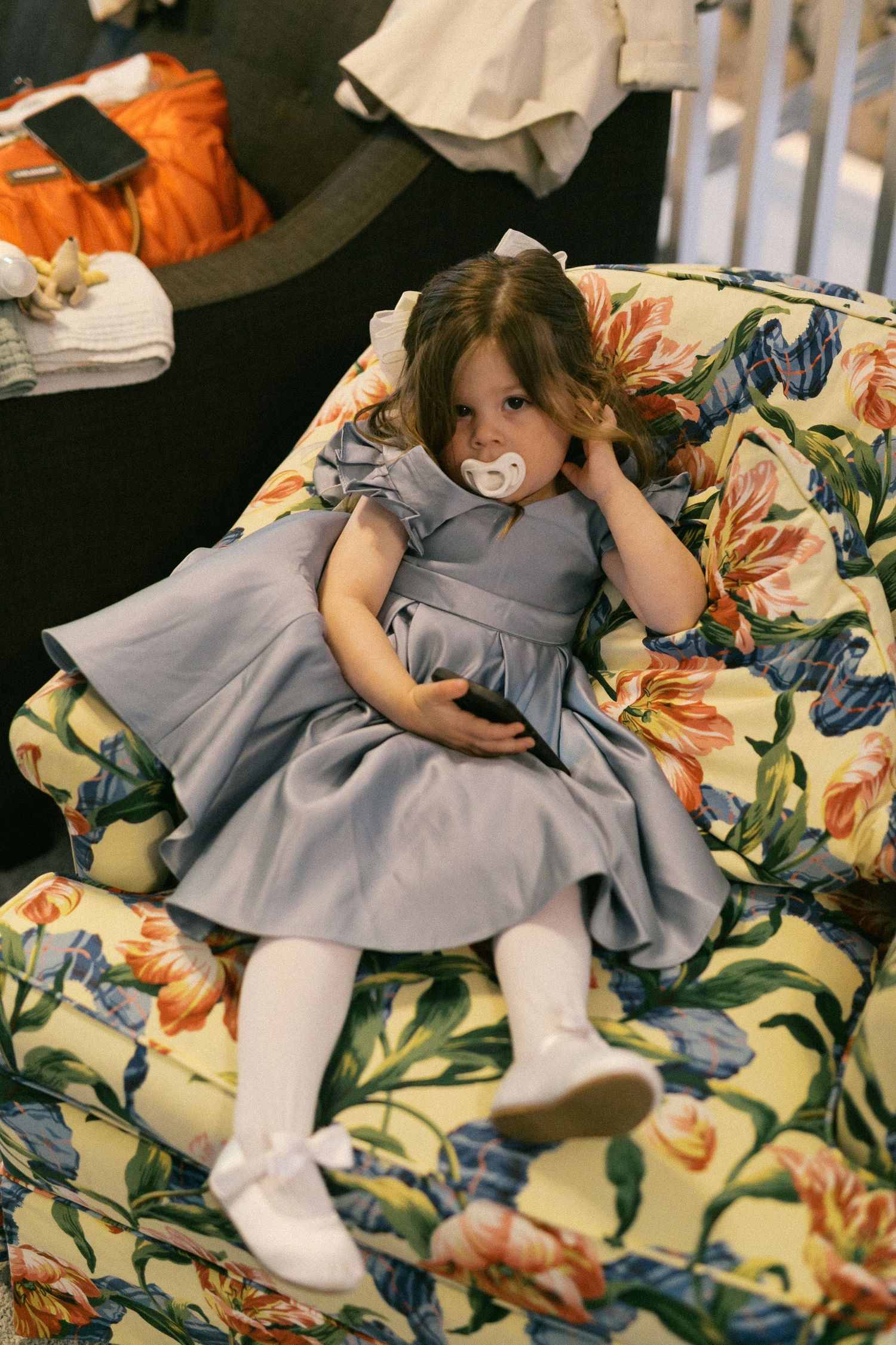 Child in gray dress rests on floral patterned couch during wedding festivities.