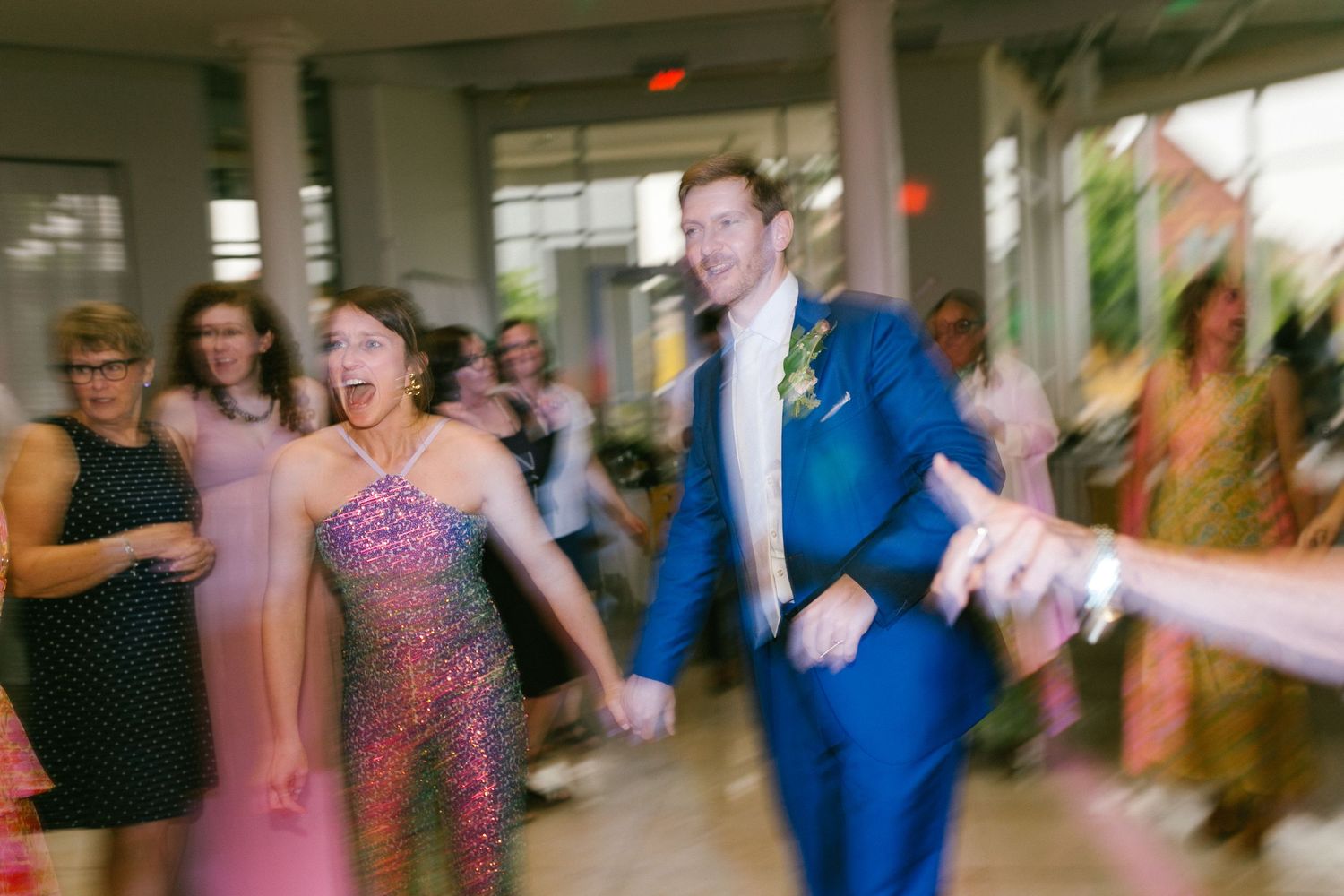 Motion-blurred shot of guests dancing together on a lively wedding reception dance floor.