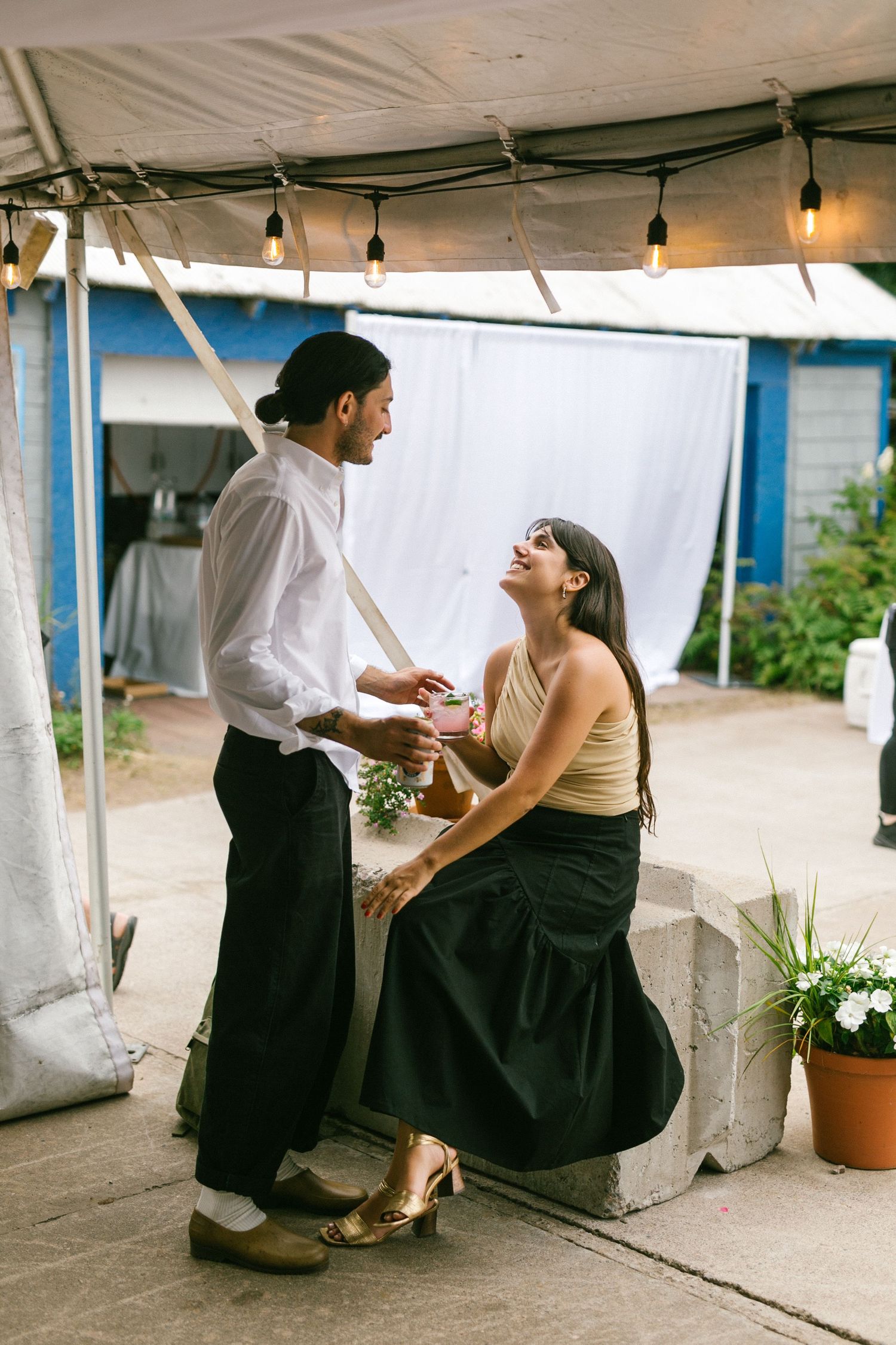 Candid moments between guests at an outdoor event under a white tent with string lights.