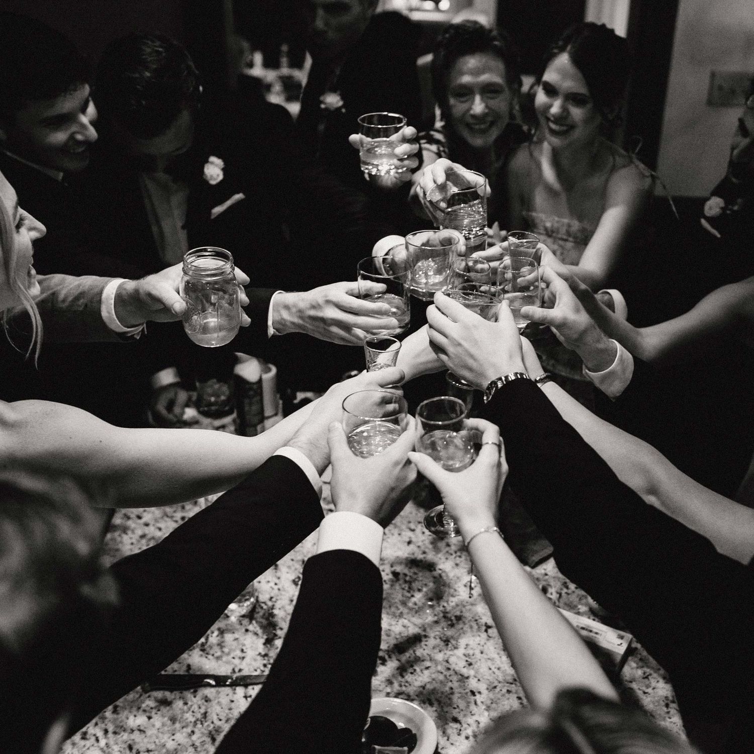 Black and white photo of a wedding party toasting with glasses before a wedding ceremony.
