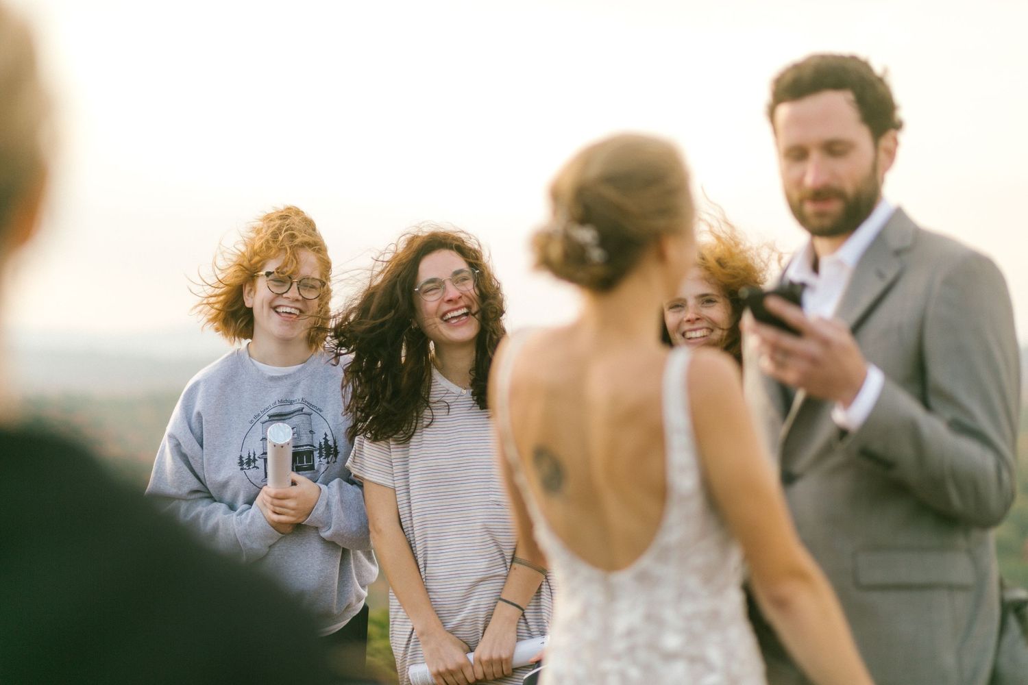 Wedding guests gather outdoors at sunset to celebrate and take photos.