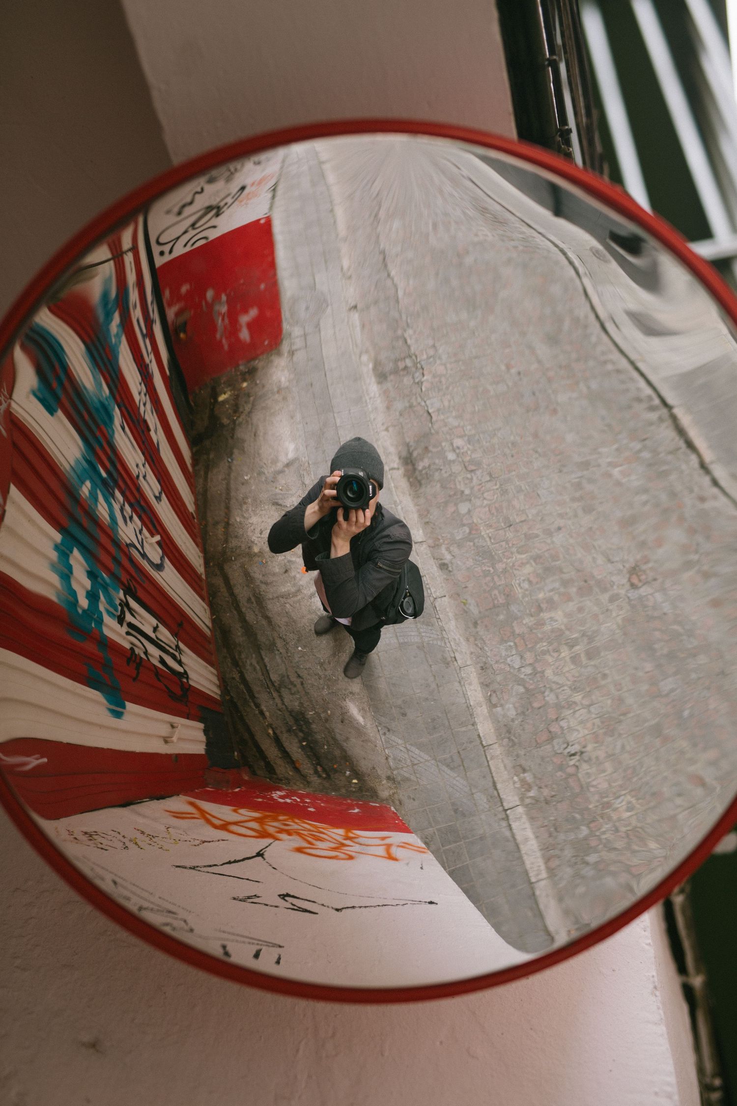 Creative reflection in a red convex safety mirror shows a photographer crouched down taking a picture from above.