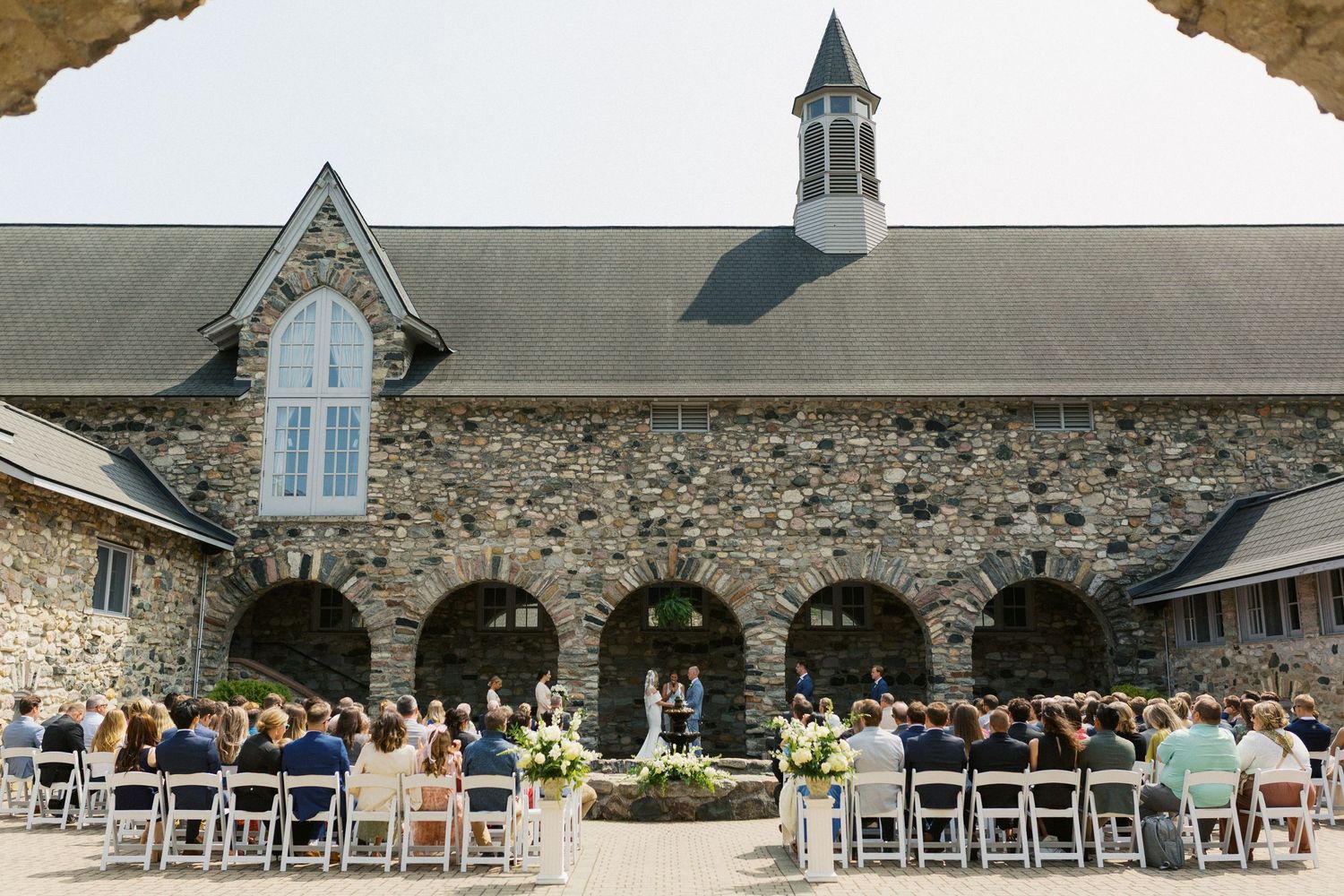 Stone church exterior with spire and white chairs set up for an outdoor wedding ceremony.