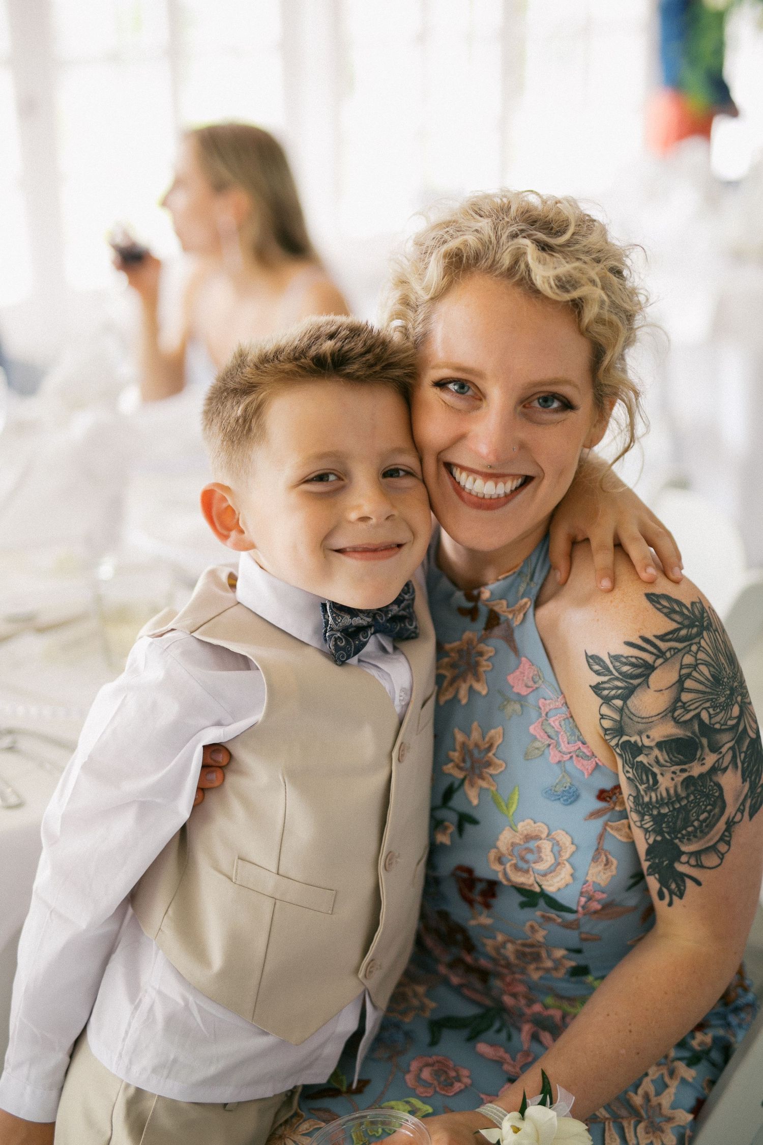 A loving candid moment featuring bright smiles and a floral dress with visible arm tattoos at a formal event.